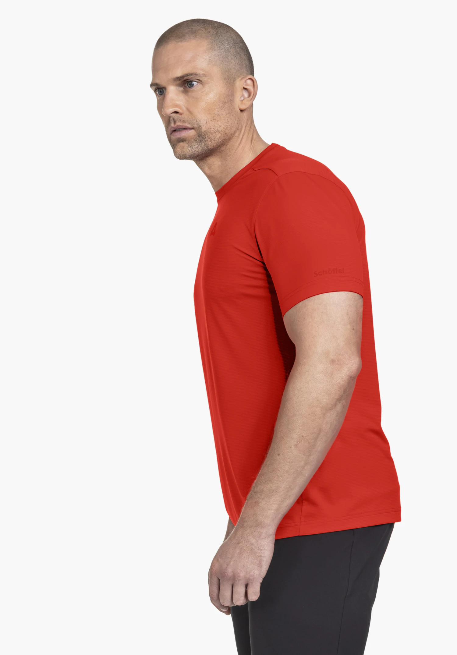 T Shirt Style Chipoma MEN in een heldere oranje kleur. Het model staat zijwaarts voor een neutrale achtergrond en presenteert het shirt, waarbij het subtiele Schöffel-logo op de mouw goed zichtbaar is.