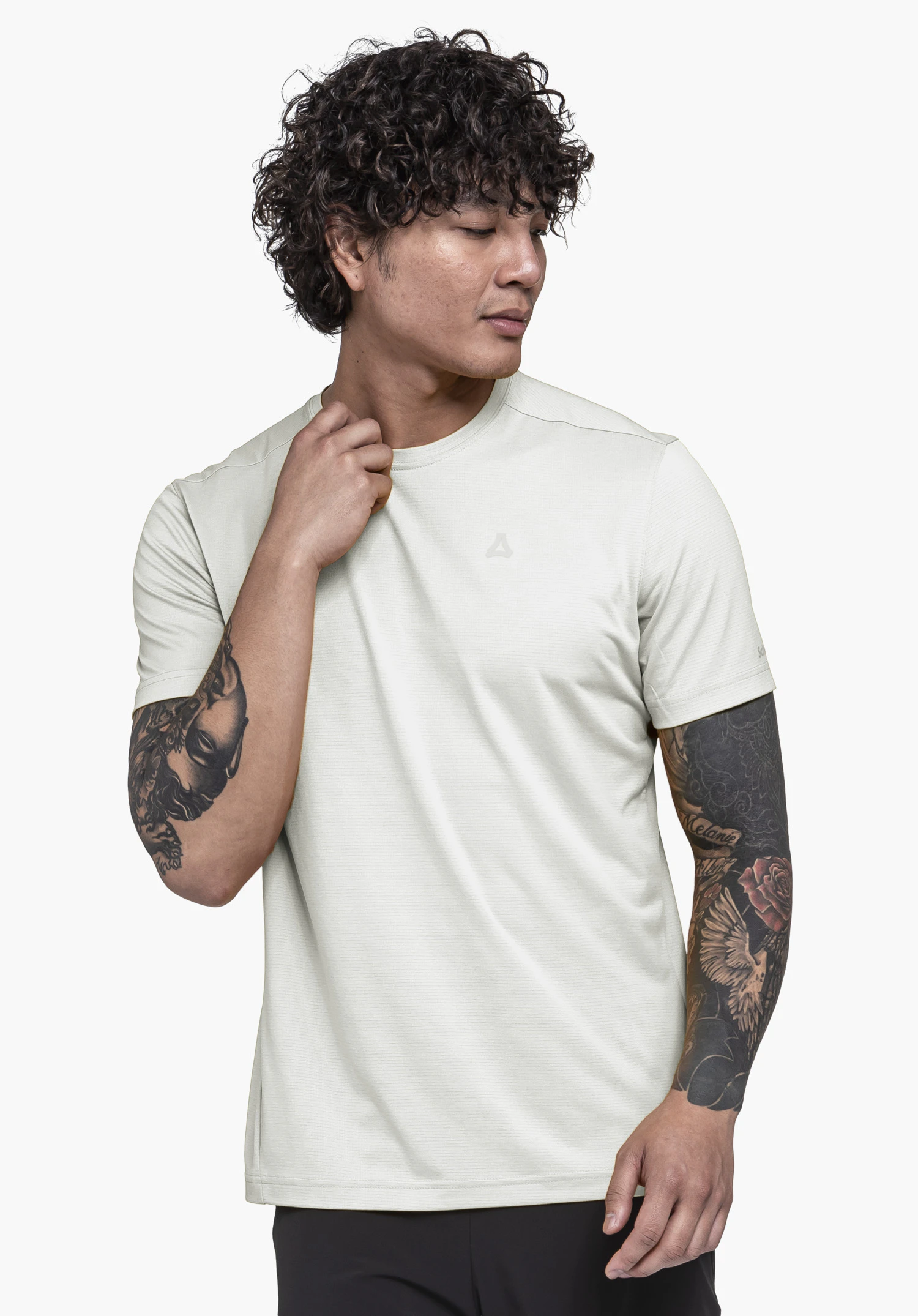 T Shirt Style Chipoma MEN in het wit. Een getatoeëerd model staat in een zijwaartse pose tegen een neutrale achtergrond en raakt de kraag aan. Het subtiele Schöffel-logo op de borst onderstreept het minimalistische ontwerp.