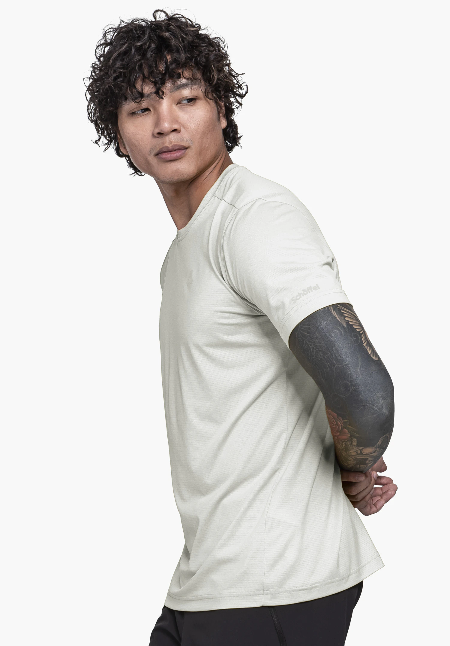 T Shirt Style Chipoma MEN in wit. Een model staat zijwaarts voor een neutrale achtergrond en kijkt over de schouder, waarbij het subtiele Schöffel-logo op de mouw goed zichtbaar is.