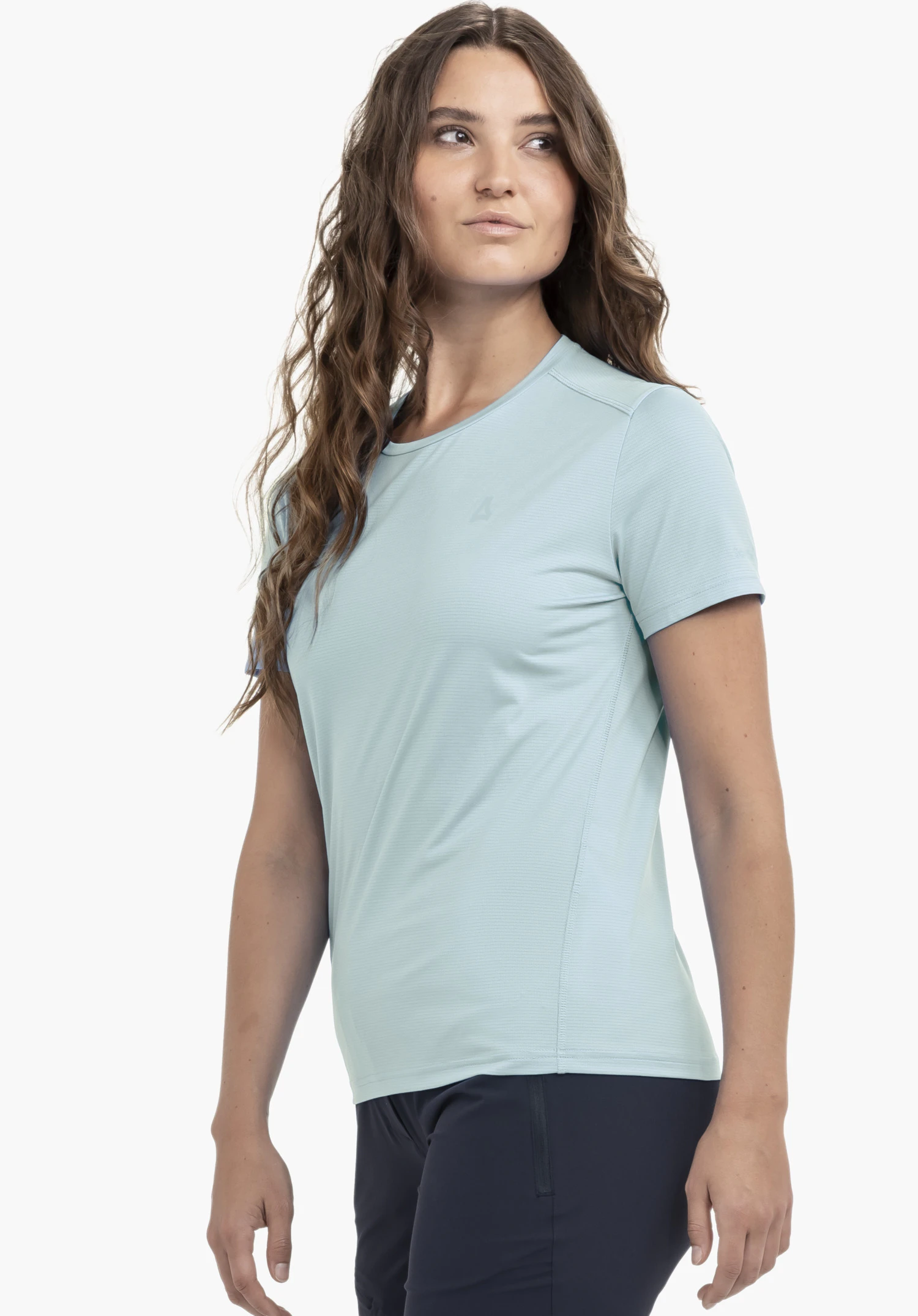 T Shirt Style Chipoma WMN in blau präsentiert vor einem neutralen Hintergrund. Das Model steht leicht seitlich versetzt und blickt über die Schulter, wodurch der feminine Schnitt gut zur Geltung kommt. Das dezente Schöffel-Logo auf der Brust ist klar zu erkennen.