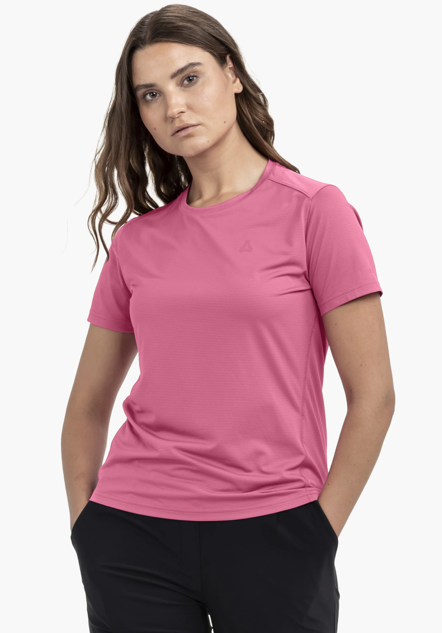 T Shirt Style Chipoma WMN in Pink. Das Model steht frontal vor einem neutralen Hintergrund und trägt das Shirt mit den Händen locker in den Taschen. Das subtile Schöffel-Logo auf der Brust verleiht dem Look eine dezente Note.