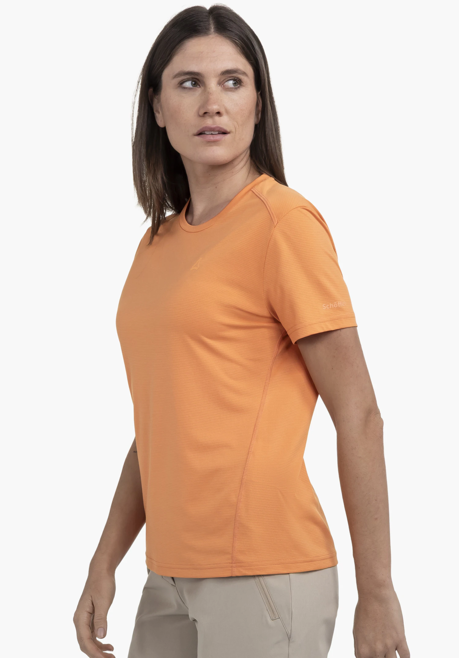 T Shirt Style Chipoma WMN in vibrant orange. The model is standing in a side-profile pose against a neutral background, showcasing the shirt and the subtle Schöffel logo on the sleeve.