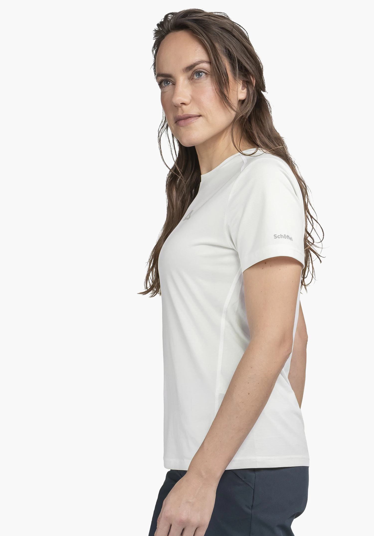 T Shirt Style Chipoma WMN en blanc : Un mannequin se tient de profil devant un fond neutre et présente ce t-shirt fonctionnel. Le logo Schöffel discret sur la manche est clairement visible.