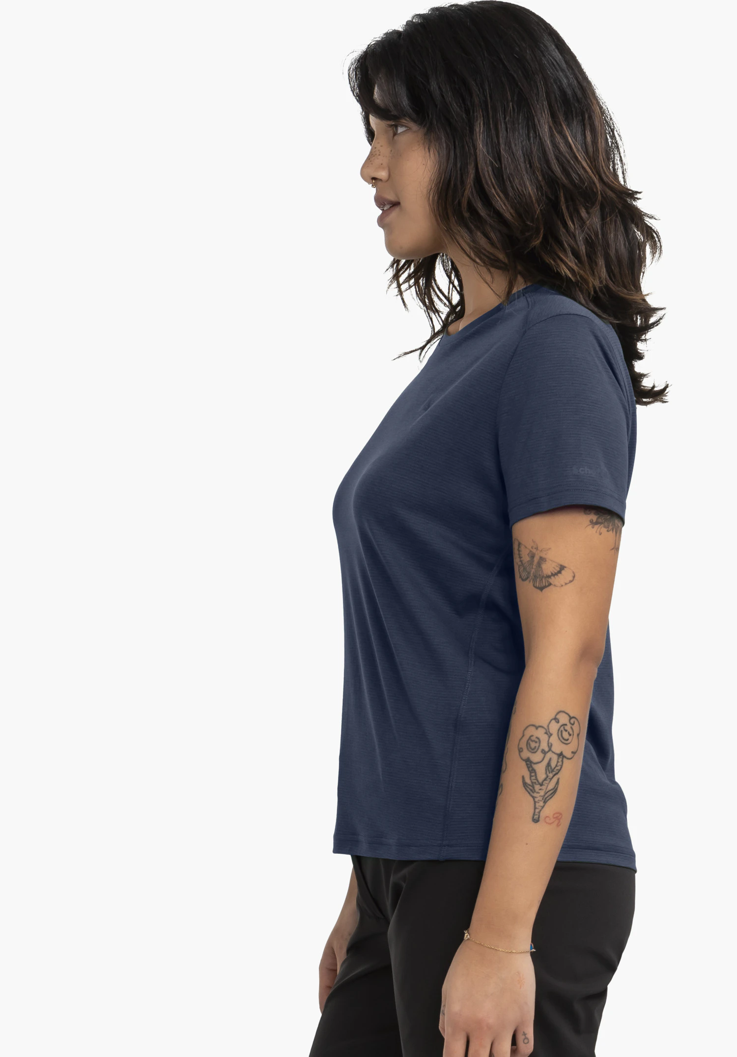 T Shirt Style Chipoma WMN: Eine Frau steht seitlich vor einem neutralen Hintergrund und präsentiert das T-Shirt in Blau. Das dezent platzierte Schöffel-Logo ist am Ärmel erkennbar.