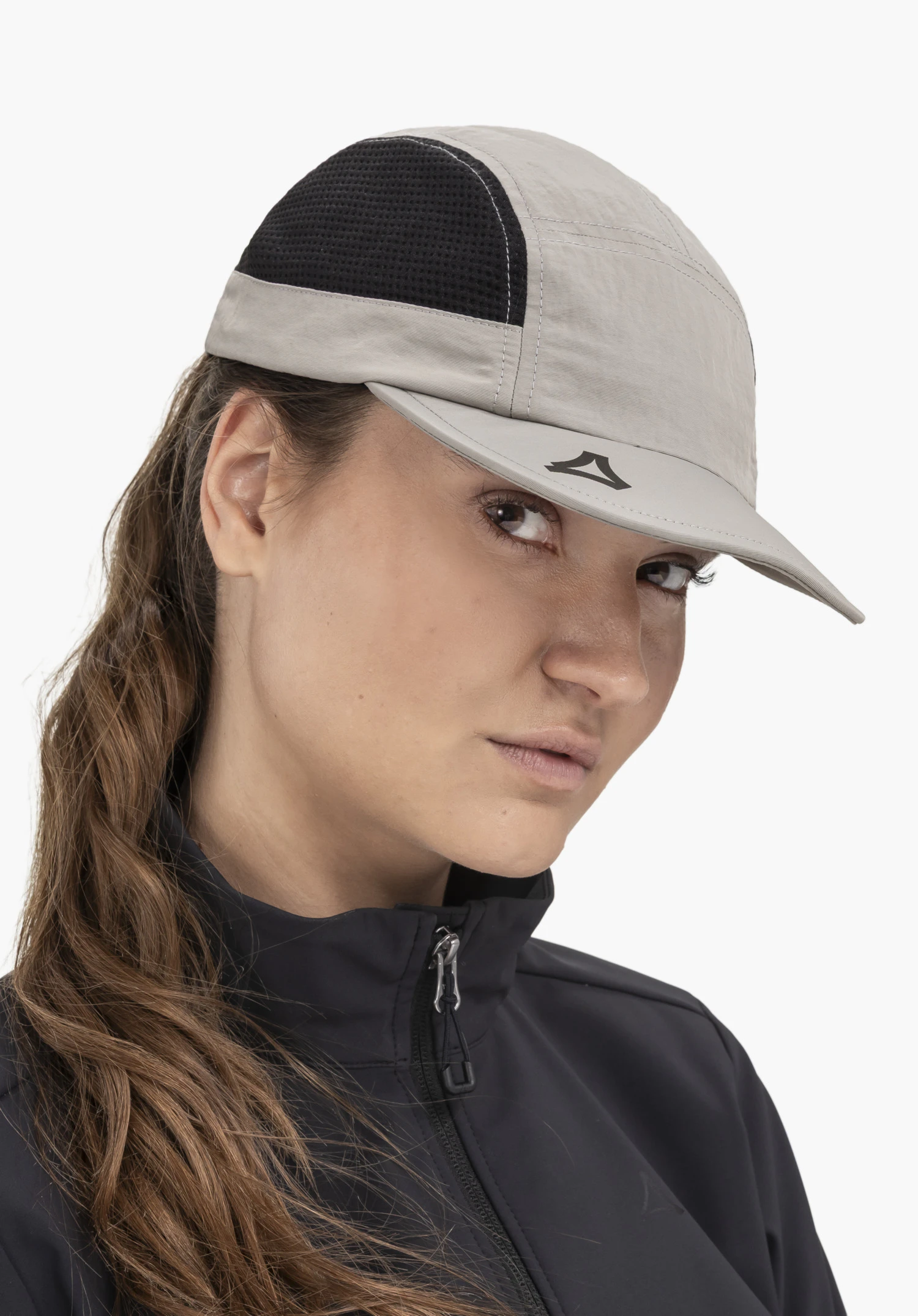 Cap Style Mauku UNI, portée par un mannequin qui se tient légèrement de profil et regarde l'appareil photo. Elle présente la casquette grise avec des empiècements noirs et le Schöffel-Logo bien visible sur la visière, photographiée devant un fond neutre.