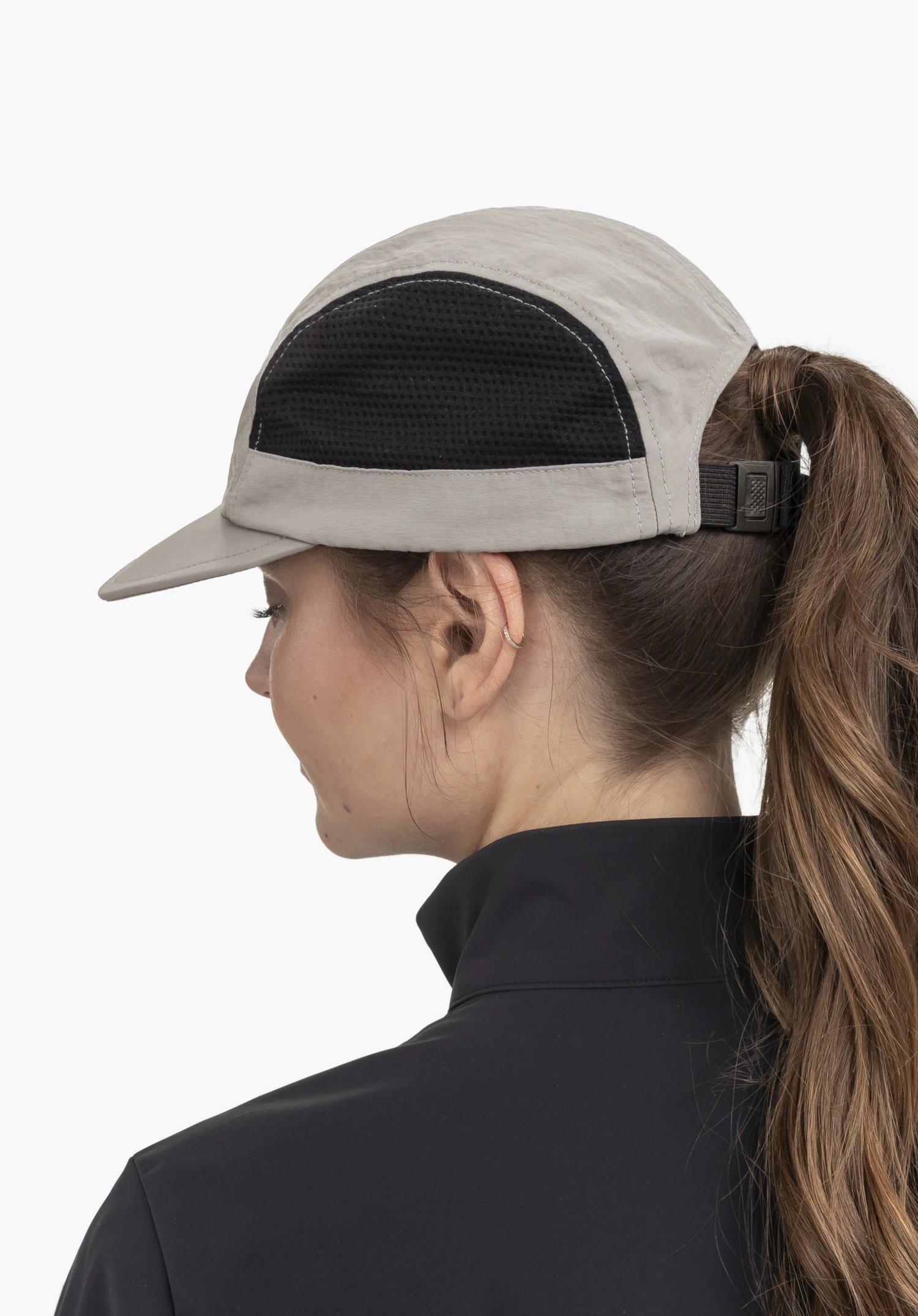 Cap Style Mauku UNI. Un mannequin se tient de profil en légère vue de dos et porte la casquette grise avec des empiècements en maille noire. L'image présente le produit sur un fond neutre.