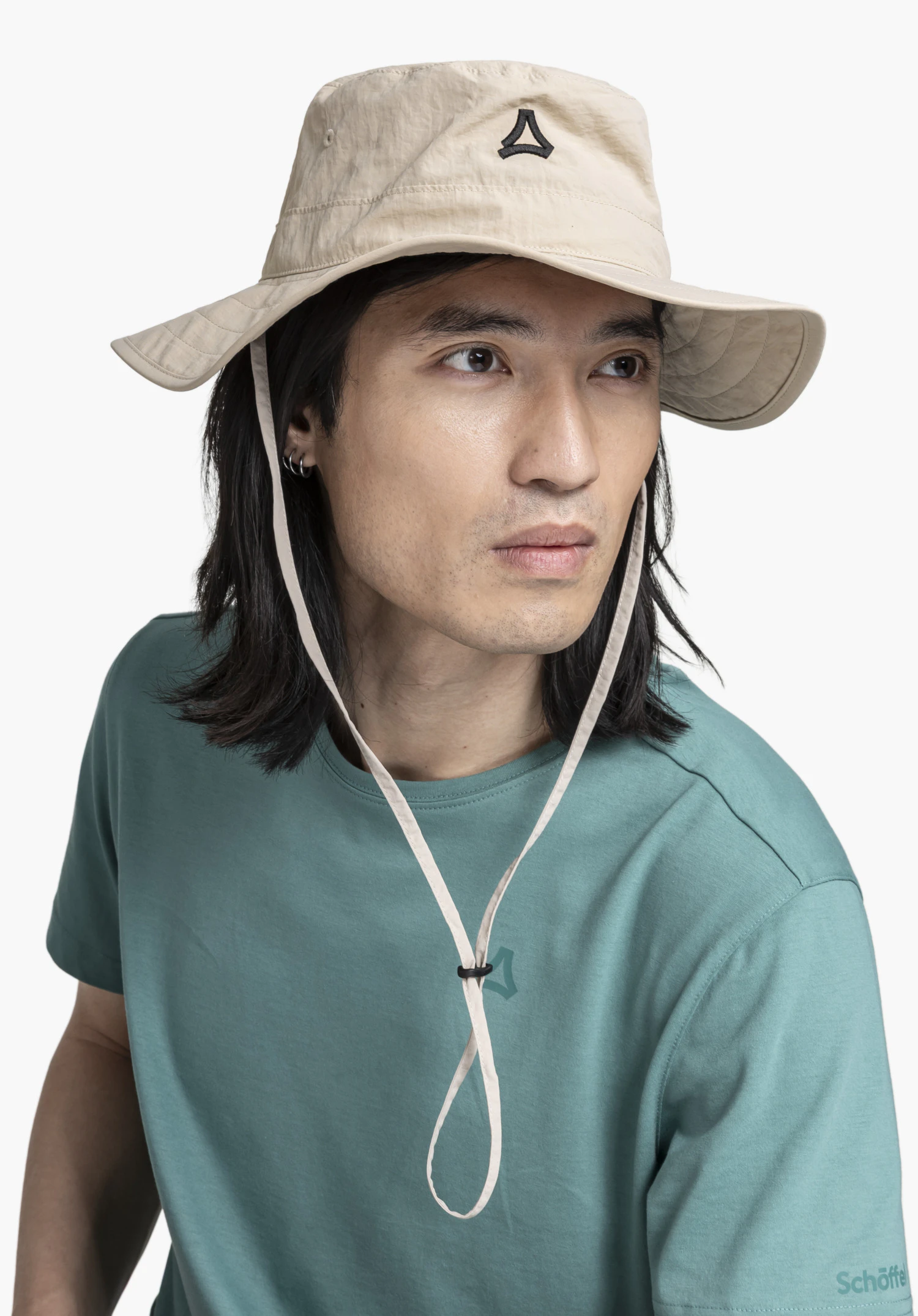 Hat Style Fraydo UNI in Beige an einem Model, das in einer seitlich gewandten Pose vor einem neutralen Hintergrund steht, wobei das Schöffel-Logo auf der Front deutlich sichtbar ist.