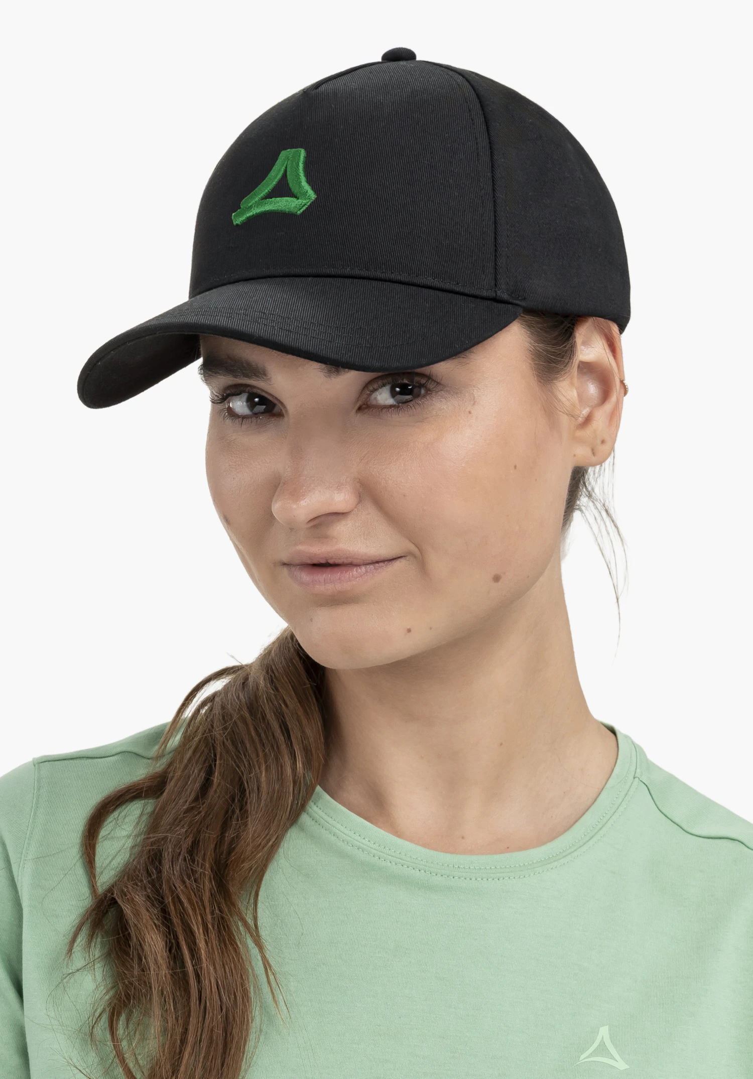 Cap Style Collada UNI in schwarz. Man sieht das Model in einer Porträtaufnahme leicht frontal stehen und direkt in die Kamera schauen, wobei das grüne Schöffel-Logo auf der Vorderseite deutlich sichtbar ist. Die Aufnahme entstand vor einem neutralen Hintergrund.