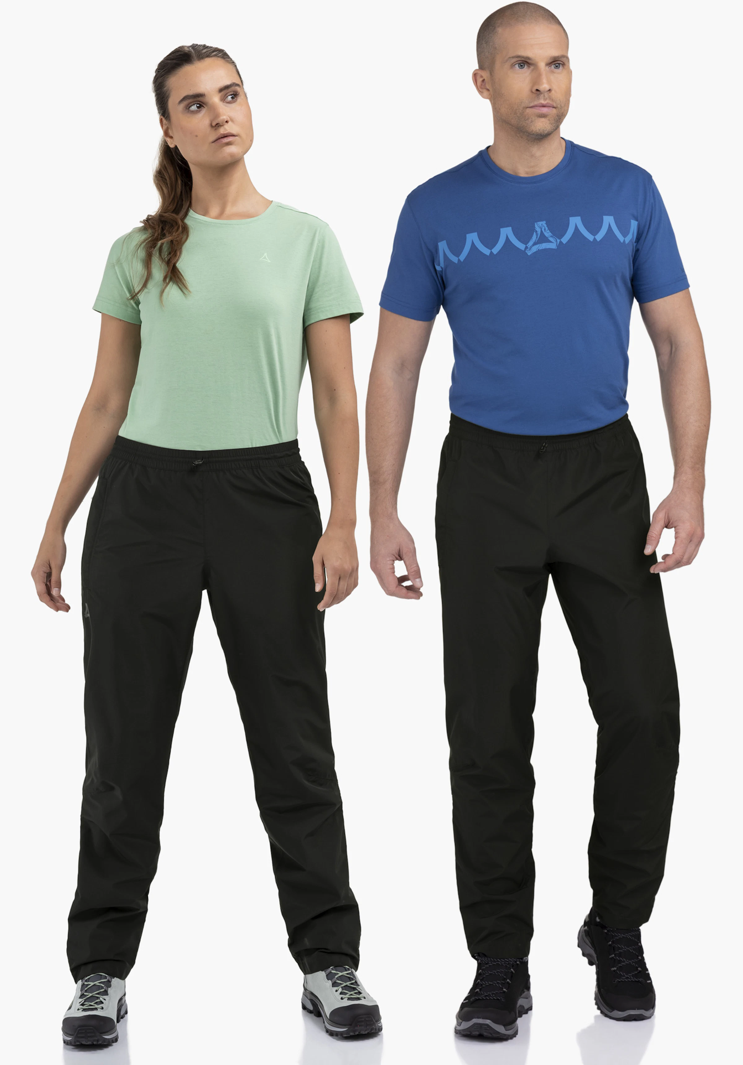 Rain Pants Style Elmori UNI in black. The model stands facing forwards and presents the rain trousers against a neutral background.