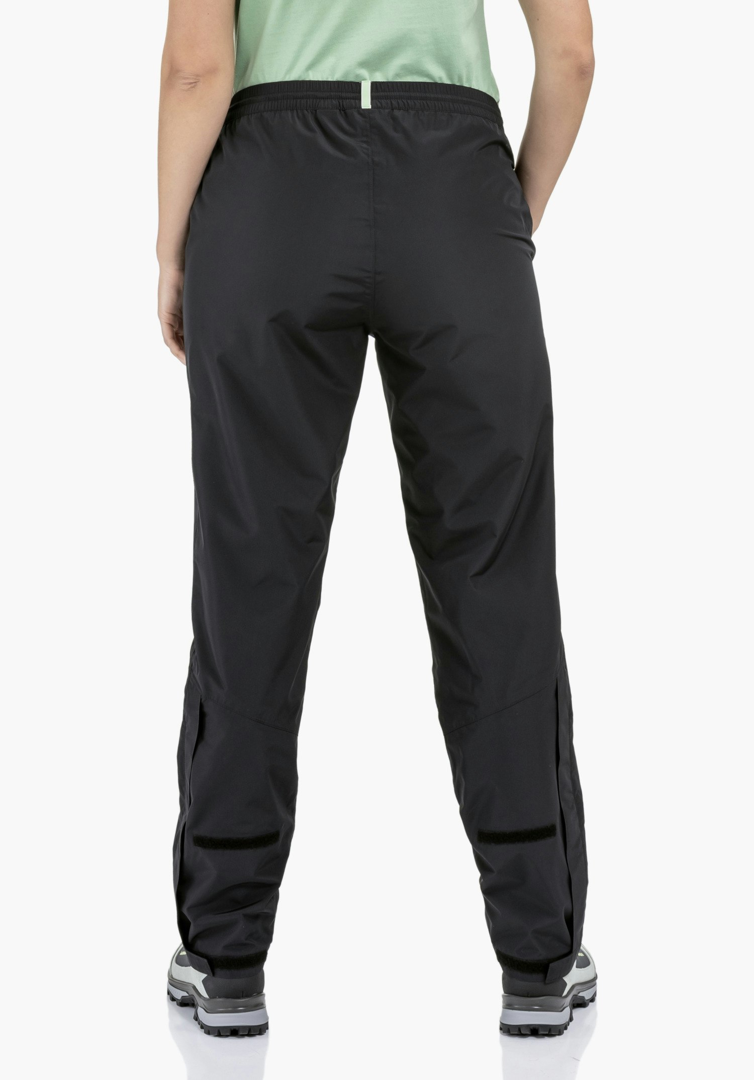 Rain Pants Style Elmori UNI shows the practical velcro fasteners for width adjustment at the lower leg hem on the smooth black fabric, ideal for an individual fit, close-up against a white/neutral background.