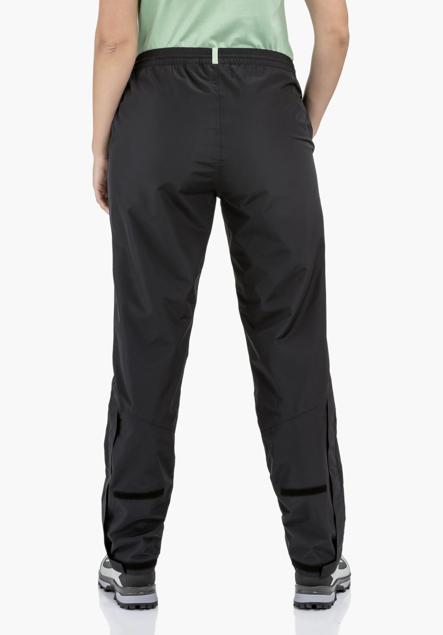 Rain Pants Style Elmori UNI shows the practical velcro fasteners for width adjustment at the lower leg hem on the smooth black fabric, ideal for an individual fit, close-up against a white/neutral background.