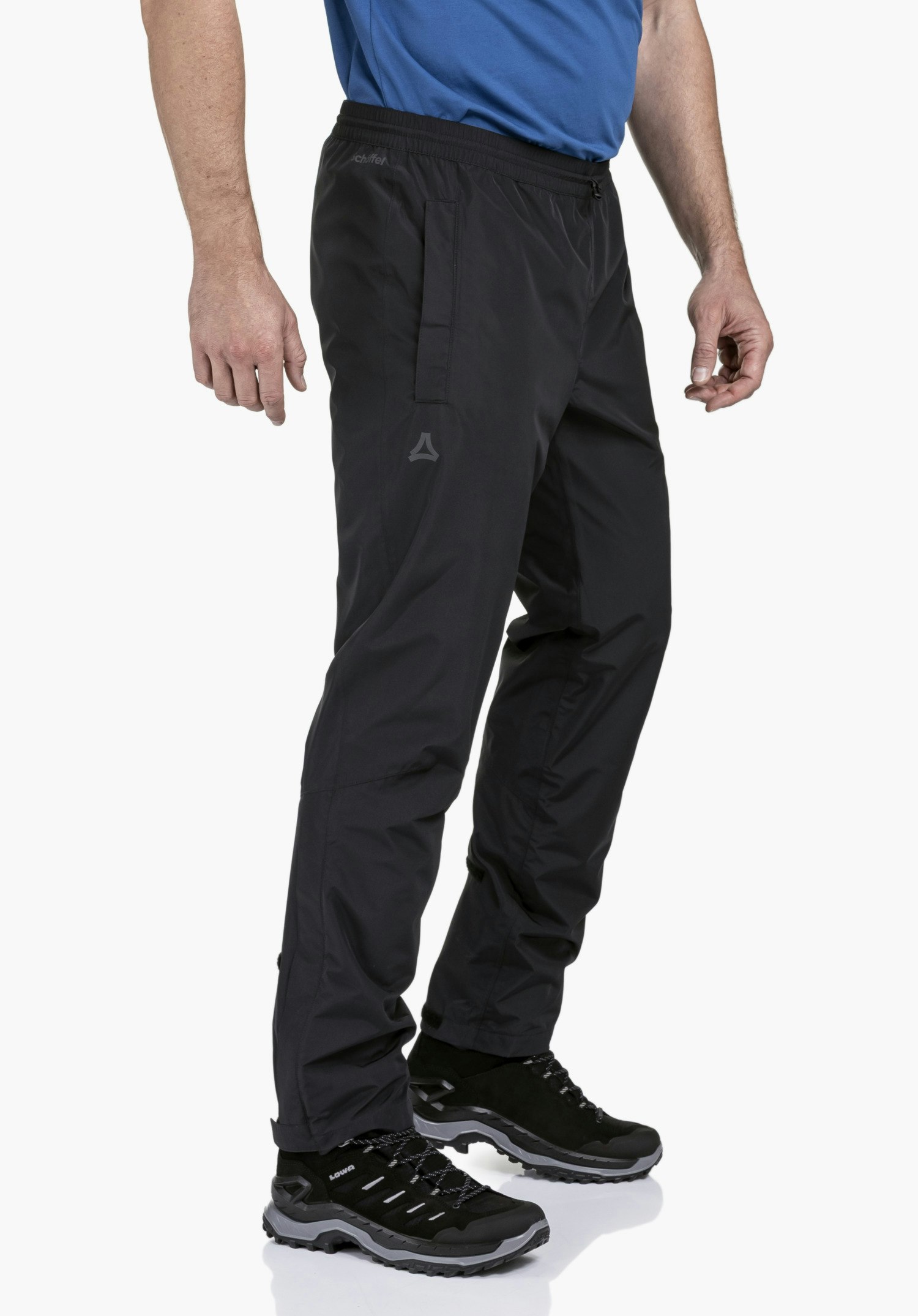 Rain Pants Style Elmori UNI in black. The model is standing sideways against a neutral background, showcasing the functional rain pants that feature the subtle Schöffel logo on the thigh and waistband.