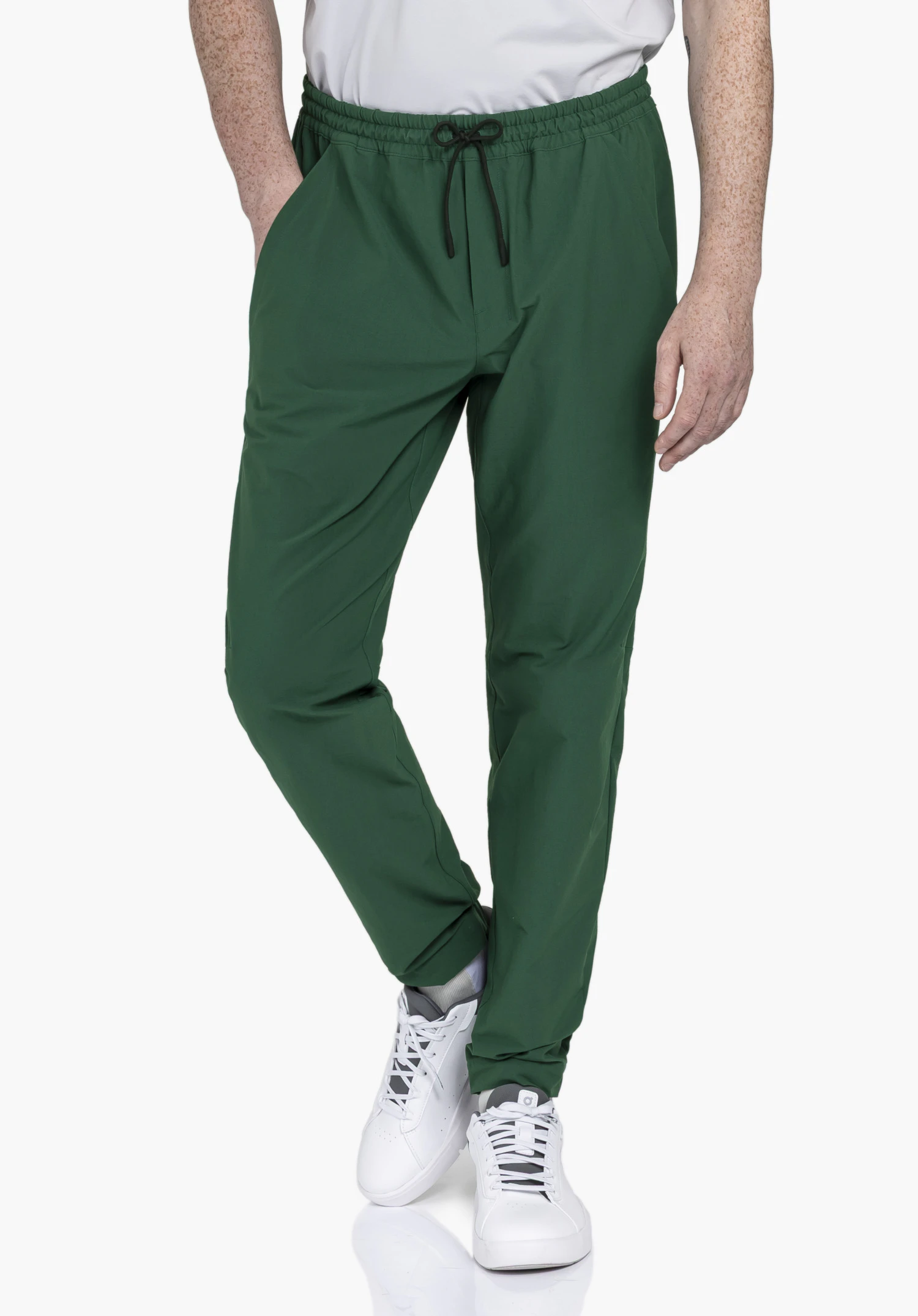 Pants Vienna M. Un mannequin présente le pantalon en vert et se tient de face, la main droite dans la poche, devant un fond neutre.