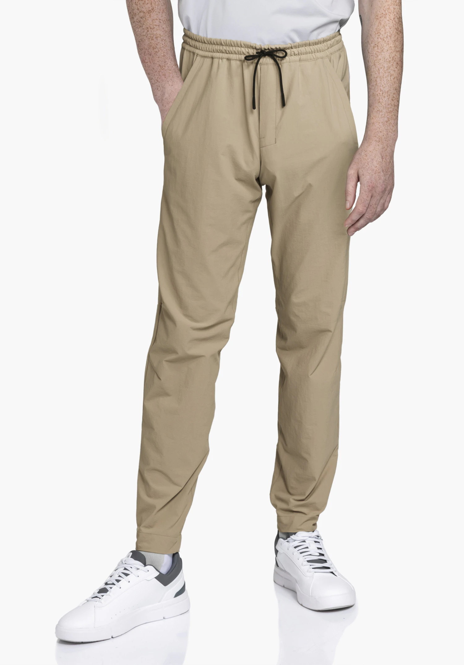 Pants Vienna M en beige sur un mannequin. Le mannequin se tient de face avec une main dans la poche, présentant le pantalon avec une taille élastique et un cordon de serrage noir devant un fond neutre.