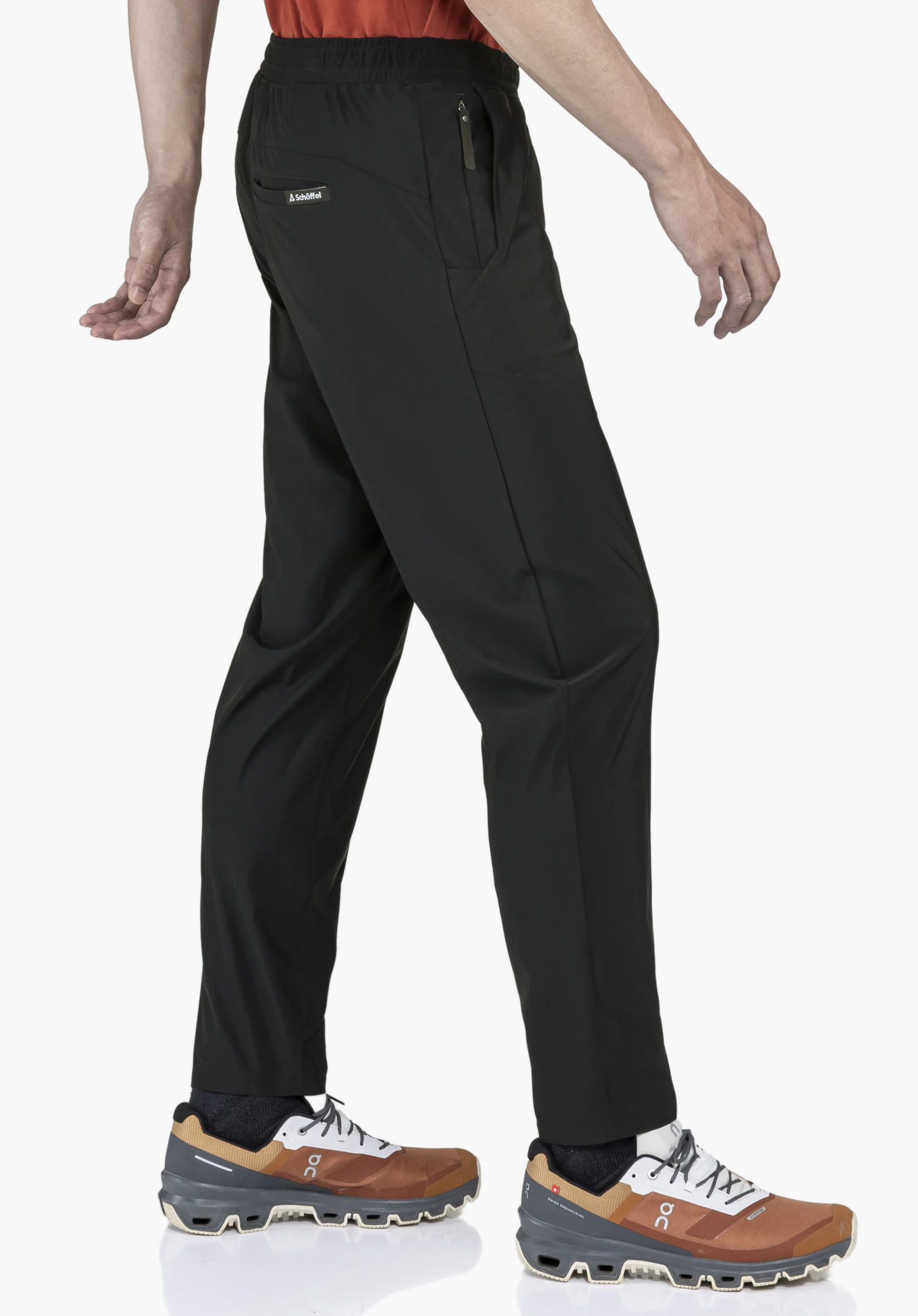 Jersey Pants Style Calmay MEN en noir classique. Le mannequin est présenté dans une vue latérale dynamique devant un fond neutre, ce qui met parfaitement en valeur la coupe moderne du pantalon. Le logo Schöffel discrètement placé sur la poche arrière souligne le design haut de gamme.