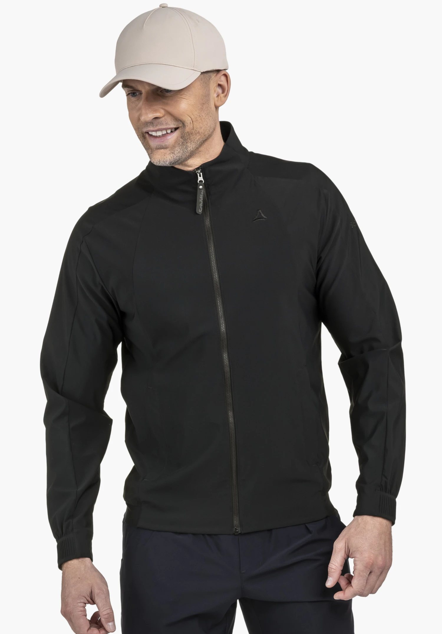 Jersey Jk Style Calmay MEN : Un mannequin souriant porte la veste noire, photographié de trois-quarts devant un fond neutre. Le logo Schöffel discret est visible sur la poitrine et souligne le design haut de gamme.