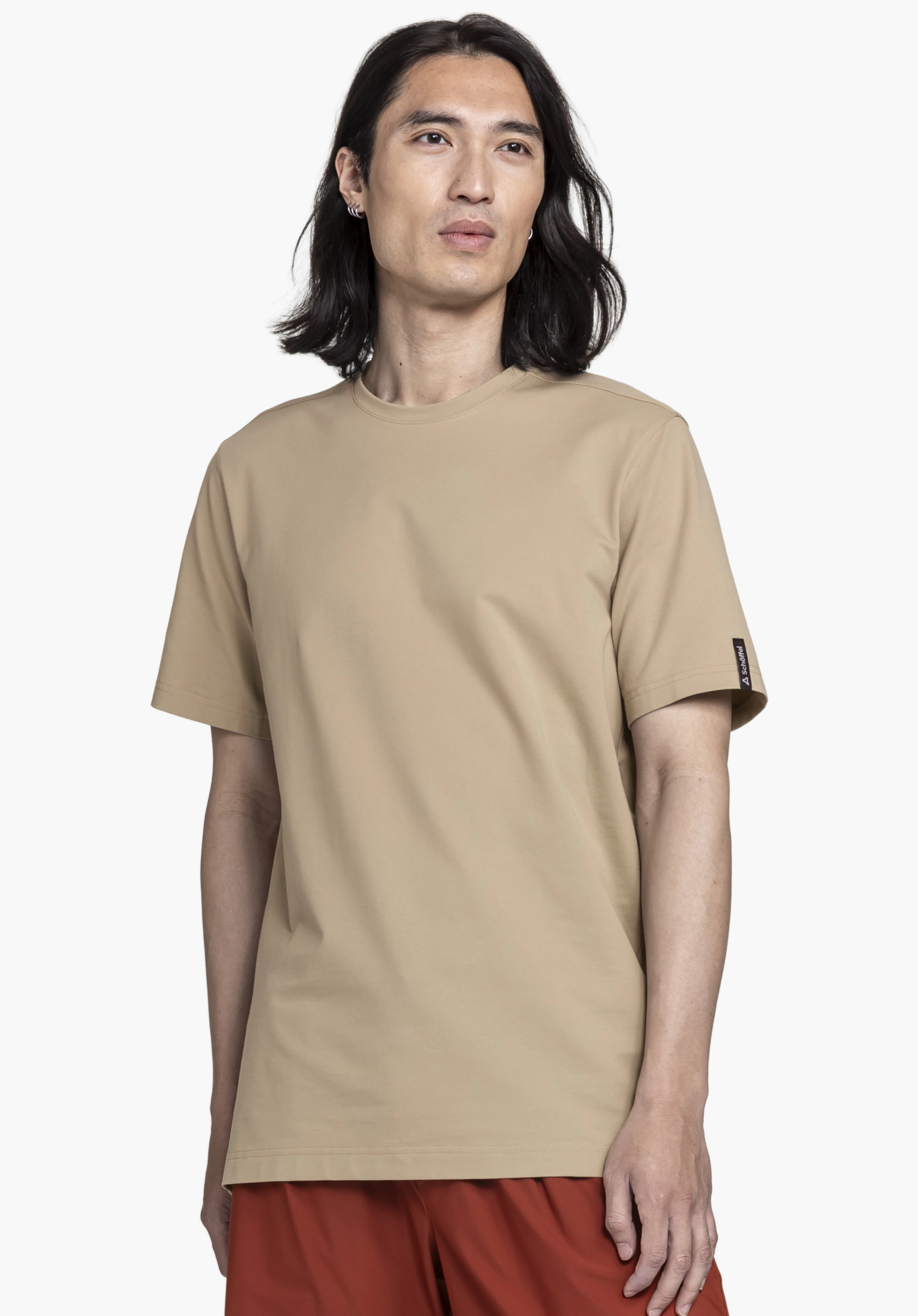 T Shirt Style Serenio MEN in beige, showcased by a model looking straight at the camera. The minimalist t-shirt stands out with its subtle color and a small, clearly visible Schöffel logo on the sleeve. The image is captured against a neutral background.