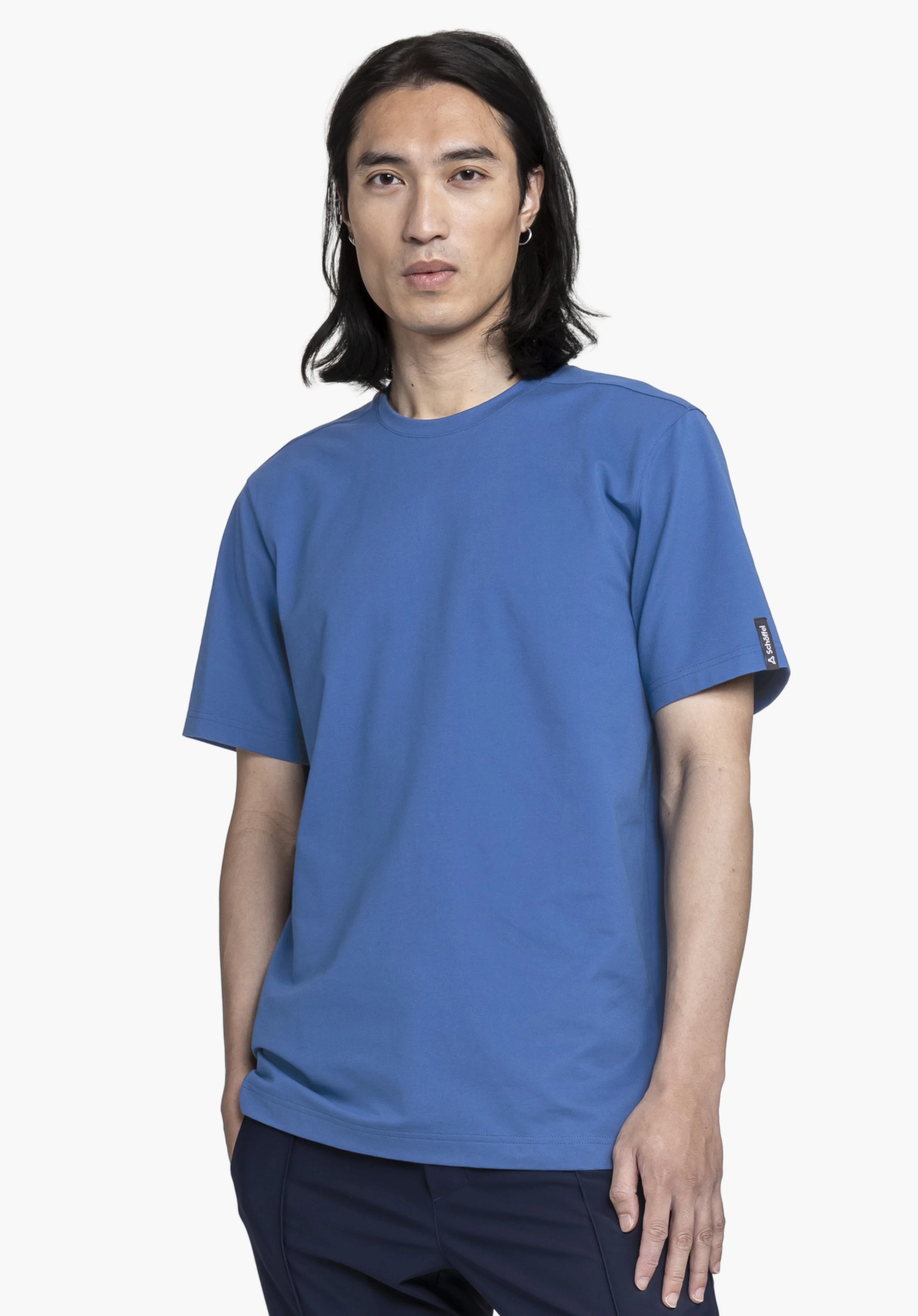 T Shirt Style Serenio MEN in Blau: Das Model steht frontal vor einem neutralen Hintergrund und präsentiert das schlichte T-Shirt. Ein dezentes Schöffel-Logo ist am Ärmel als Label-Detail erkennbar.