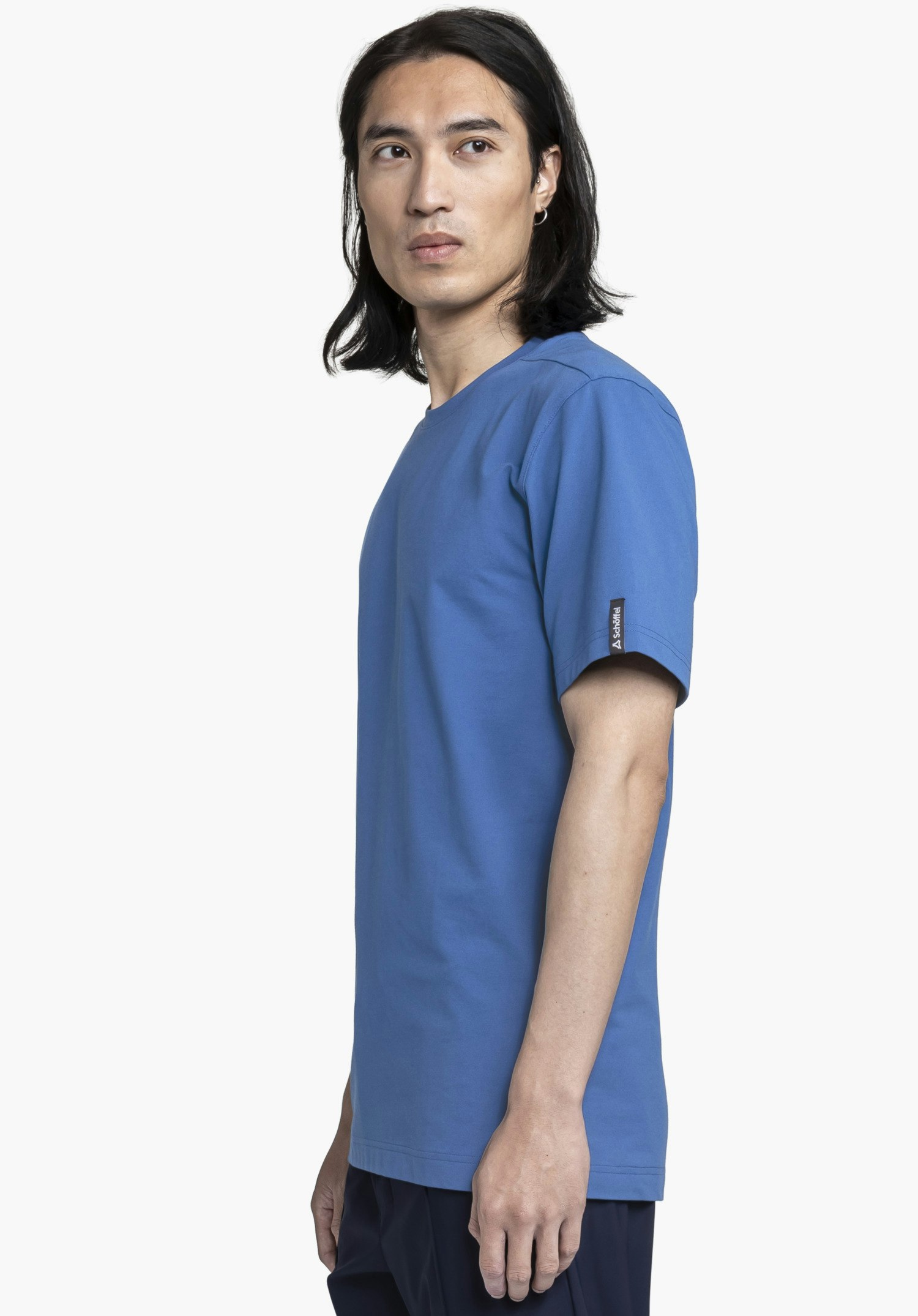 T Shirt Style Serenio MEN: Ein Model steht seitlich zum Betrachter und präsentiert das T-Shirt in einem leuchtenden Blau. Am Ärmel ist ein kleines Schöffel-Logo als Label platziert. Die Aufnahme erfolgt vor einem neutralen Hintergrund.