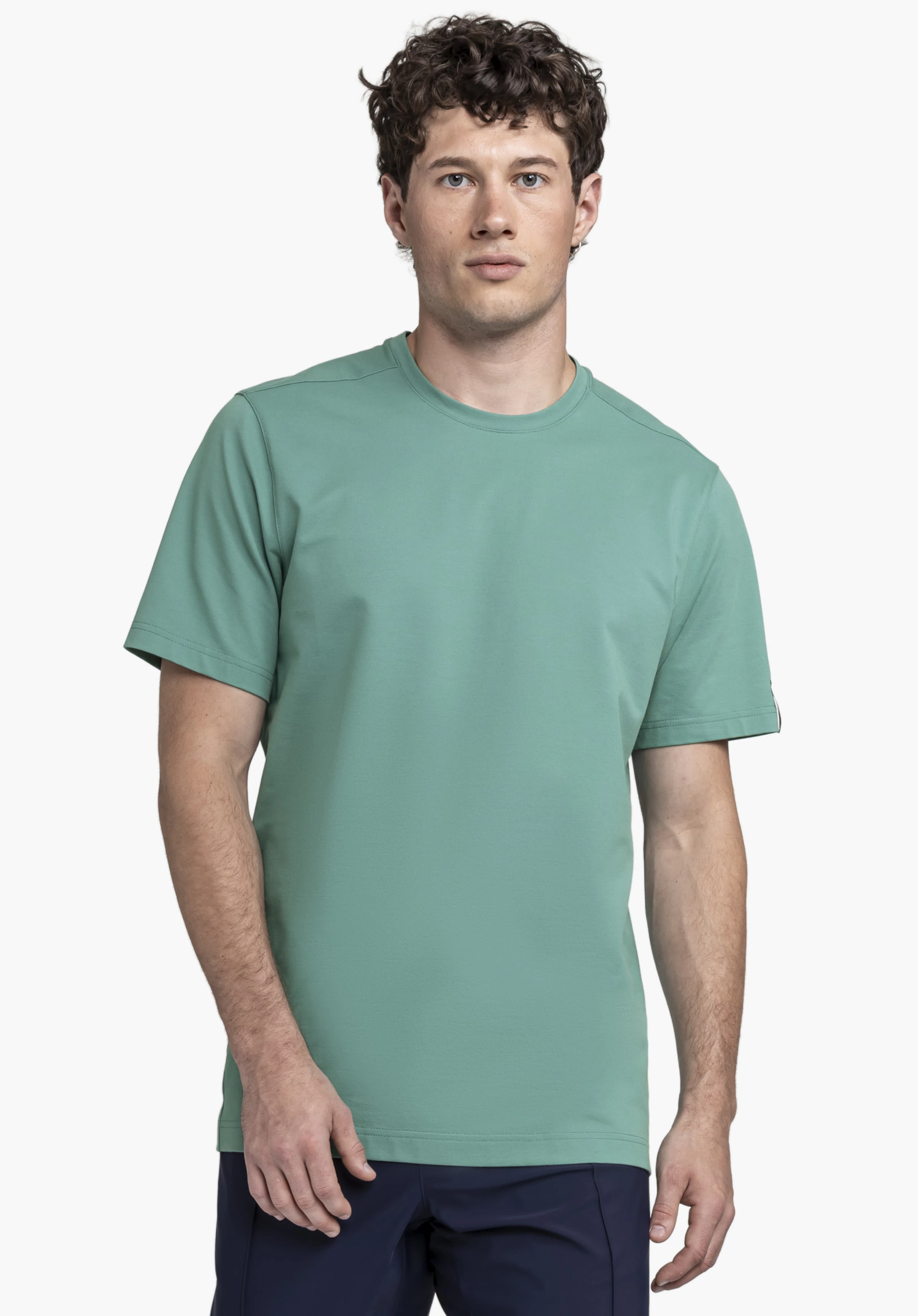 T Shirt Style Serenio MEN shown in green. The model stands facing the camera against a neutral background, highlighting the garment featuring a subtle Schöffel logo on the sleeve.