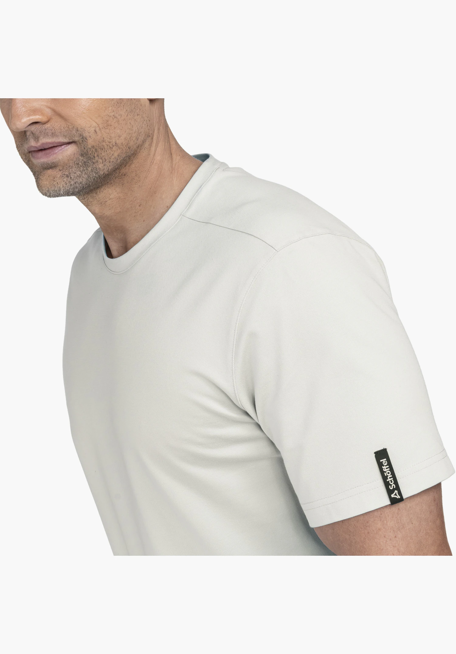 T Shirt Style Serenio MEN, focus on the black label with the Schöffel-Logo on the sleeve of the grey fabric, close-up shot against a white/neutral background.