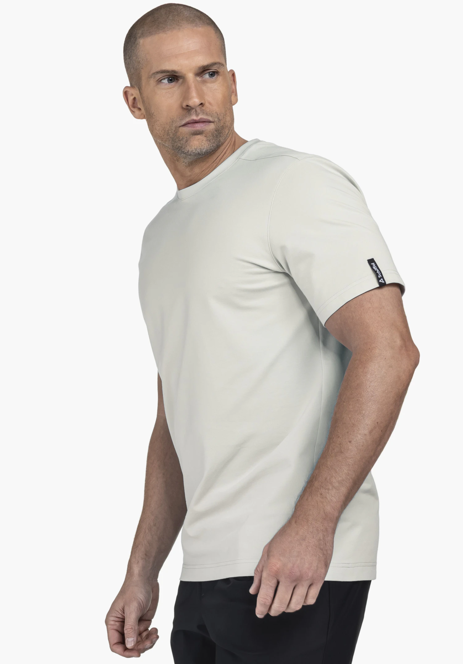 T Shirt Style Serenio MEN in grey. A model stands sideways to the viewer, showcasing the shirt against a neutral background. A small Schöffel logo is visible on the sleeve.