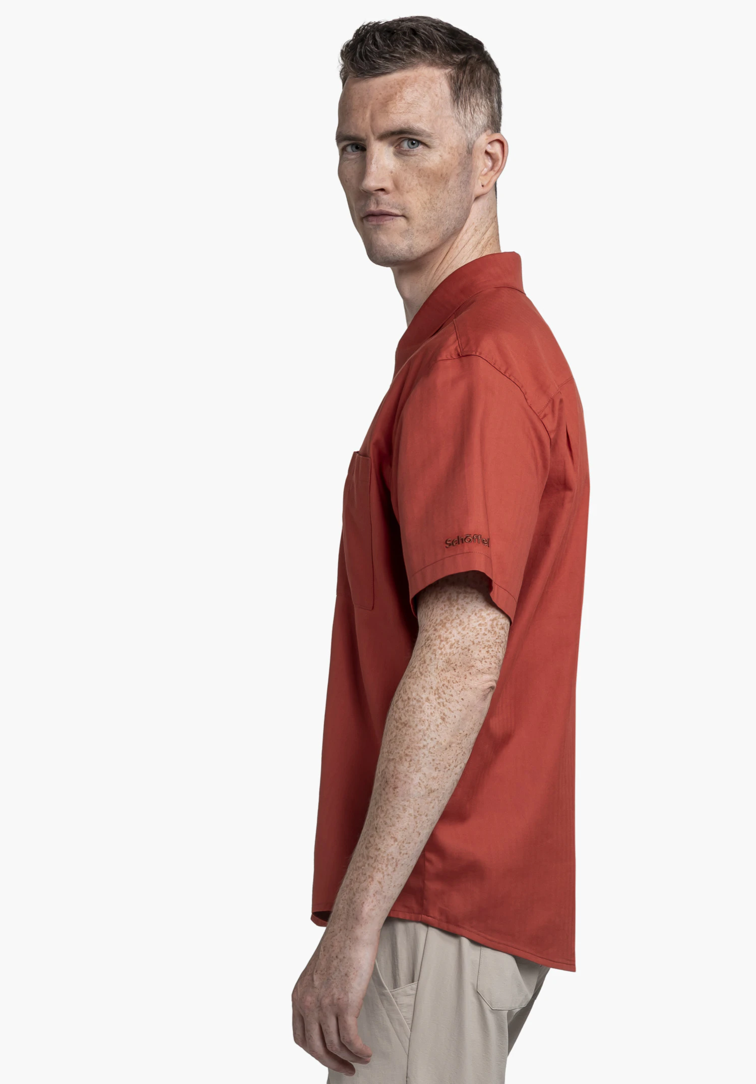 Shirt Style Kalmen MEN in Rot: Ein Model steht seitlich zu Kamera vor einem neutralen Hintergrund und präsentiert das Hemd. Das dezente Schöffel-Logo auf dem Ärmel unterstreicht den hochwertigen Look für das Winter-Outfit.