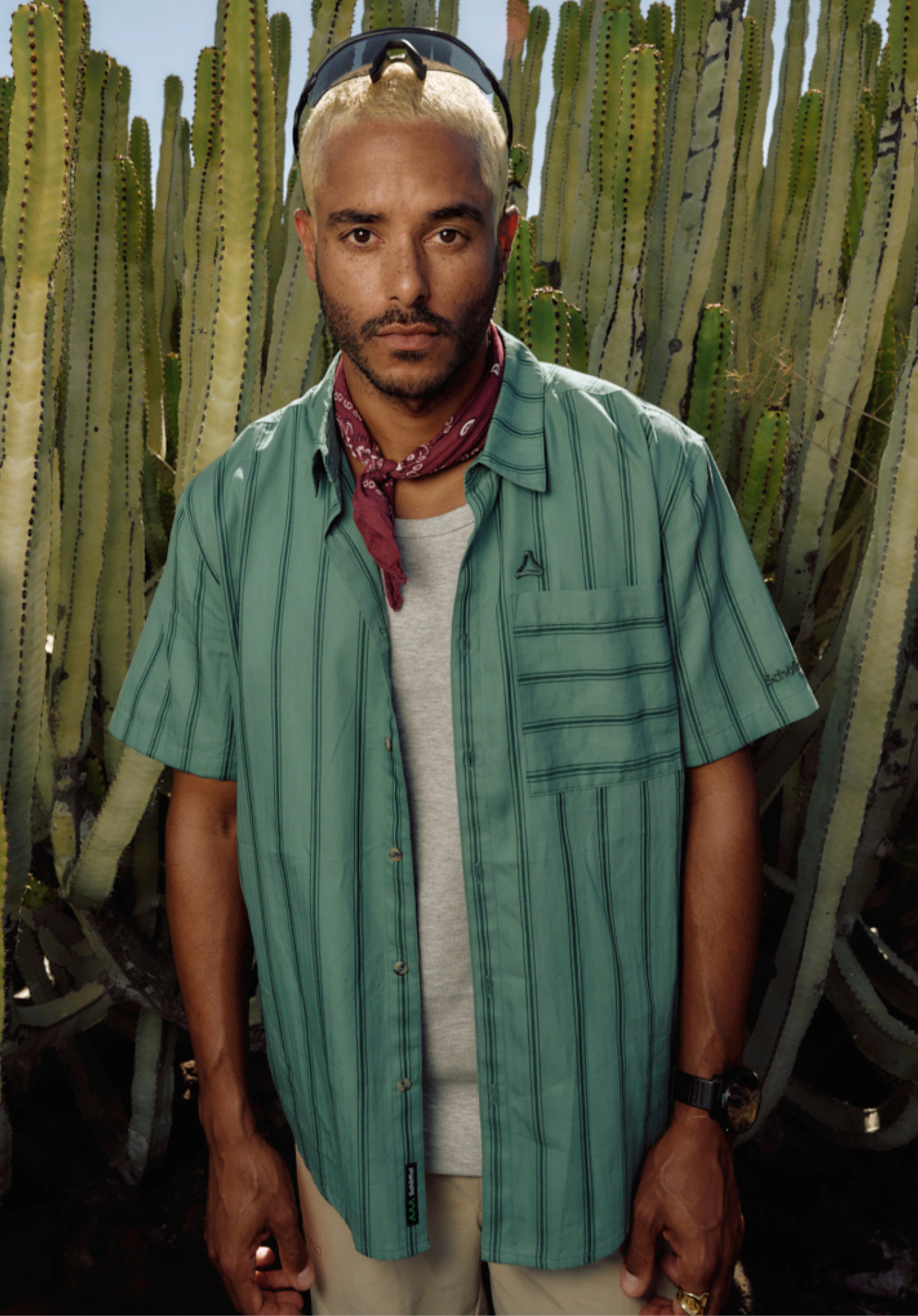 Shirt Style Kalmen MEN in green. A male model stands front-on against a neutral background wearing the short-sleeved shirt with a vertical stripe pattern. The small, subtle Schöffel logo is visible on the chest pocket and the lower hem.