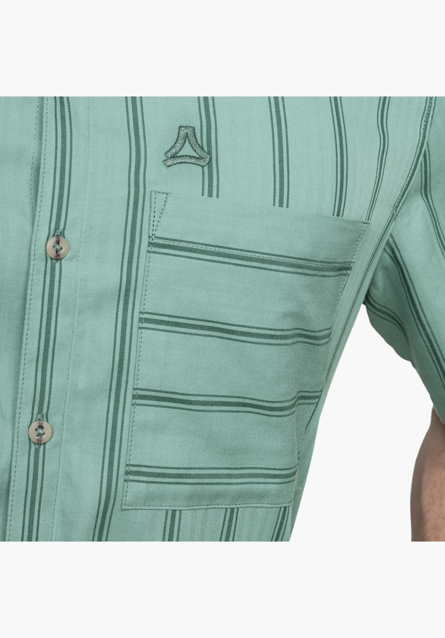 Shirt Style Kalmen MEN shows the embroidered Schöffel-Logo above the chest pocket and the finely textured, green striped fabric with button placket. Close-up against a white/neutral background.