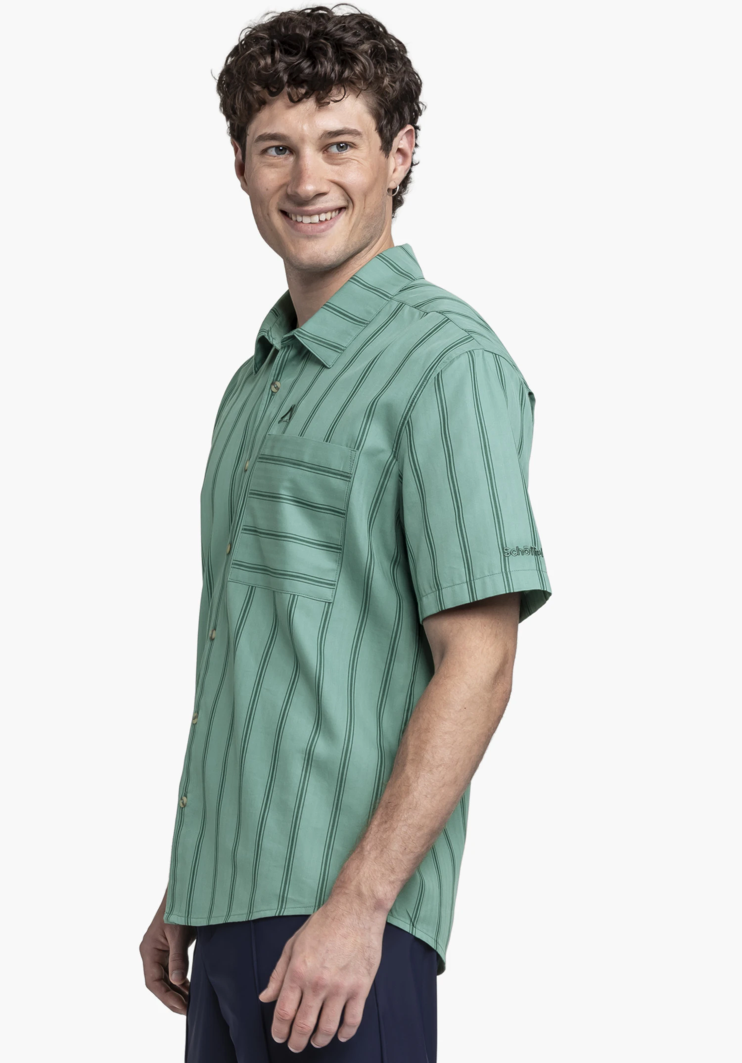 Shirt Style Kalmen MEN in green. The model stands to the side against a neutral background, showcasing the striped short-sleeve shirt with a chest pocket. The subtle Schöffel logo is visible on the sleeve.