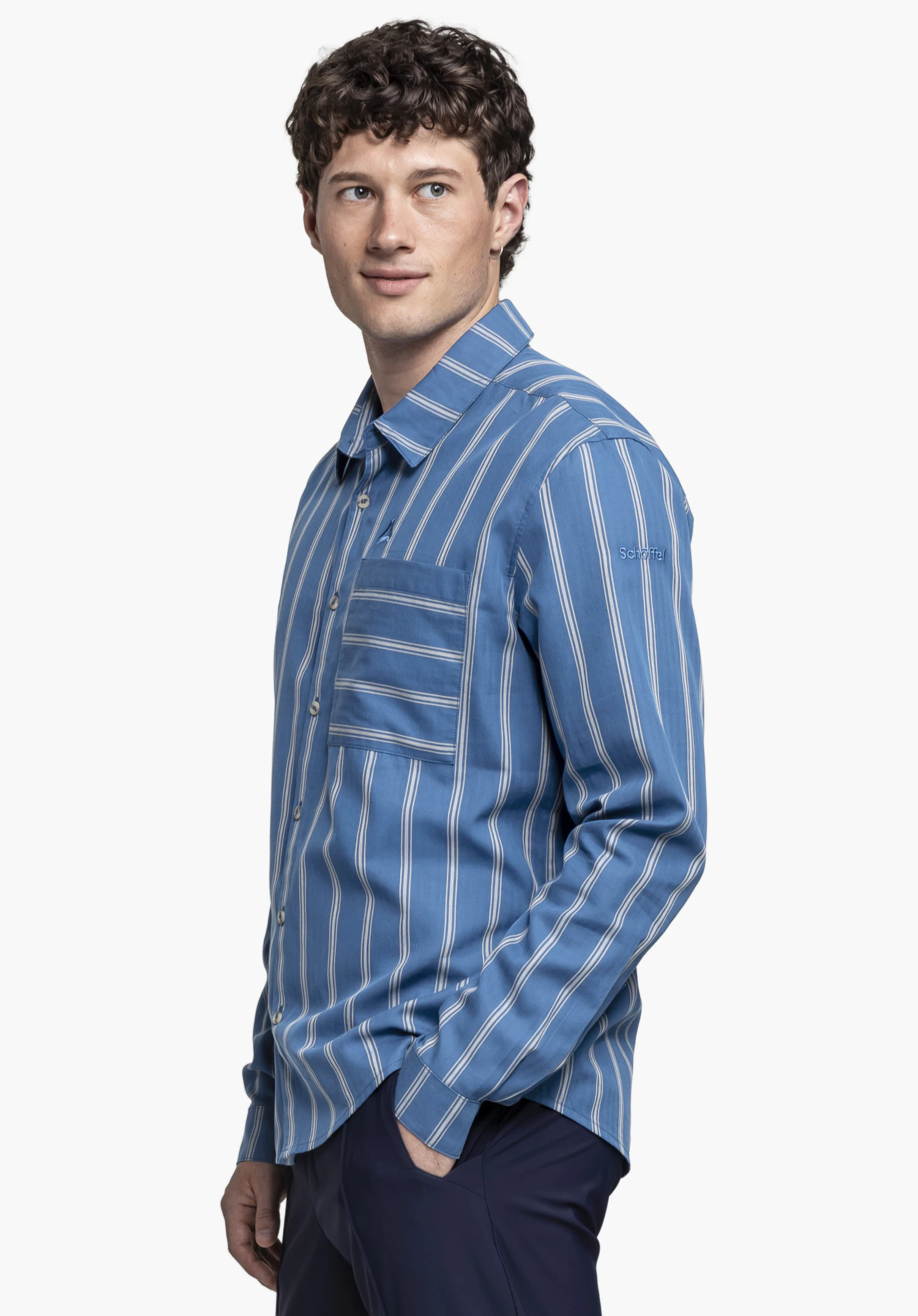 Shirt Style Chanduy MEN: The model is positioned in a side profile against a neutral background, wearing the long-sleeved shirt in blue with a subtle stripe pattern. The subtle Schöffel logo is visible on the upper left arm.