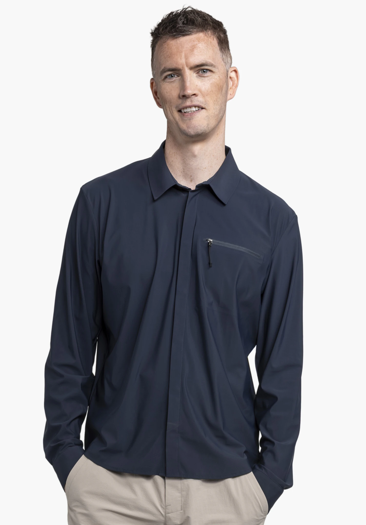 Jersey Shirt Style Calmay MEN présenté sur un modèle devant un arrière-plan neutre. Cette chemise bleue est dotée d'une poche zippée pratique sur la poitrine. Le modèle pose avec les mains dans les poches, mettant en valeur le design épuré et le col classique de cette pièce outdoor.