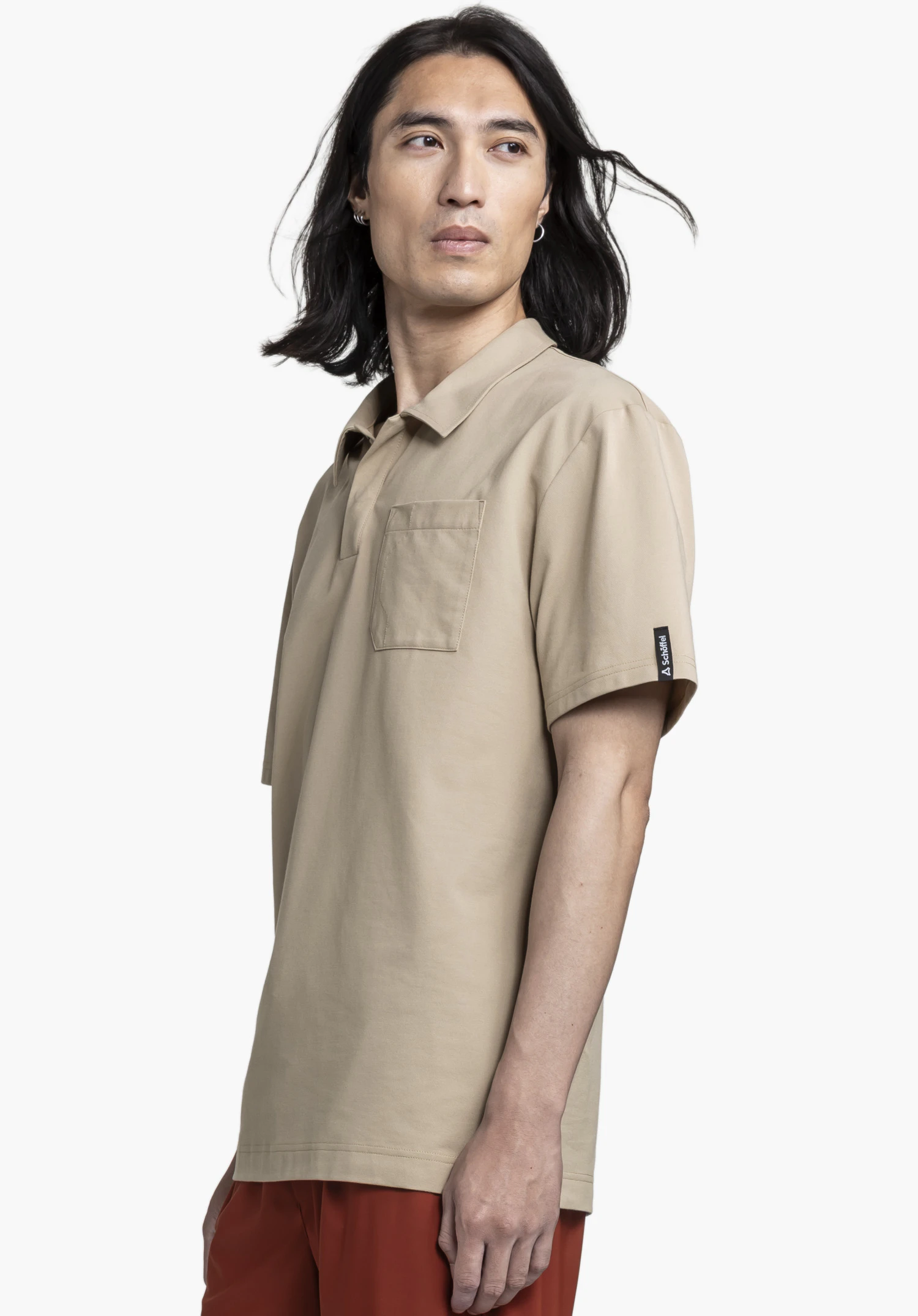 Polo Shirt Style Serenio MEN worn by a model standing sideways. The beige shirt is shown with a chest pocket and a visible Schöffel-Logo on the sleeve against a neutral background.