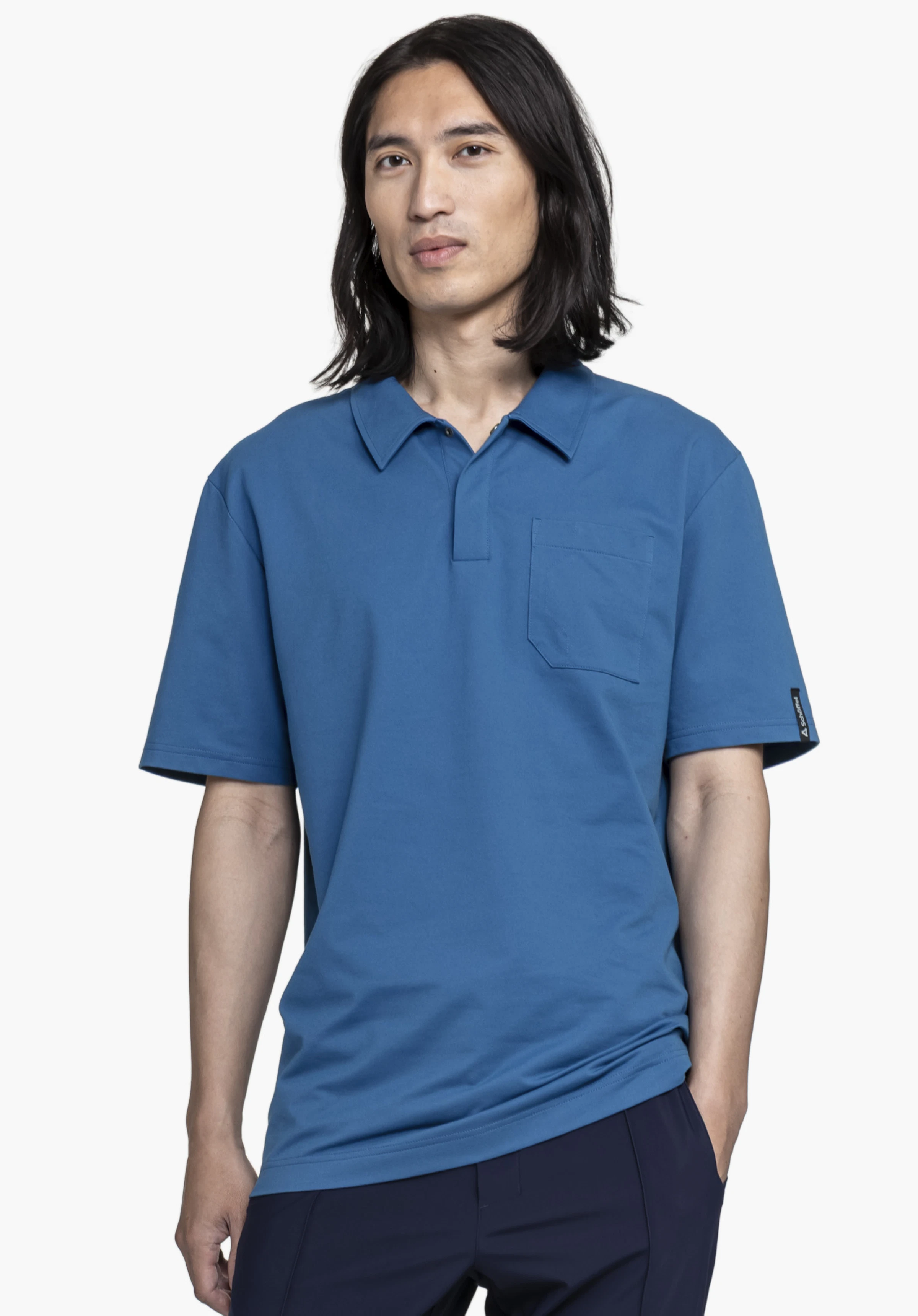 Polo Shirt Style Serenio MEN, worn by a model standing facing forward. The blue short-sleeved polo features a classic collar, a chest pocket and a small Schöffel-Logo on the left sleeve, photographed against a neutral background.