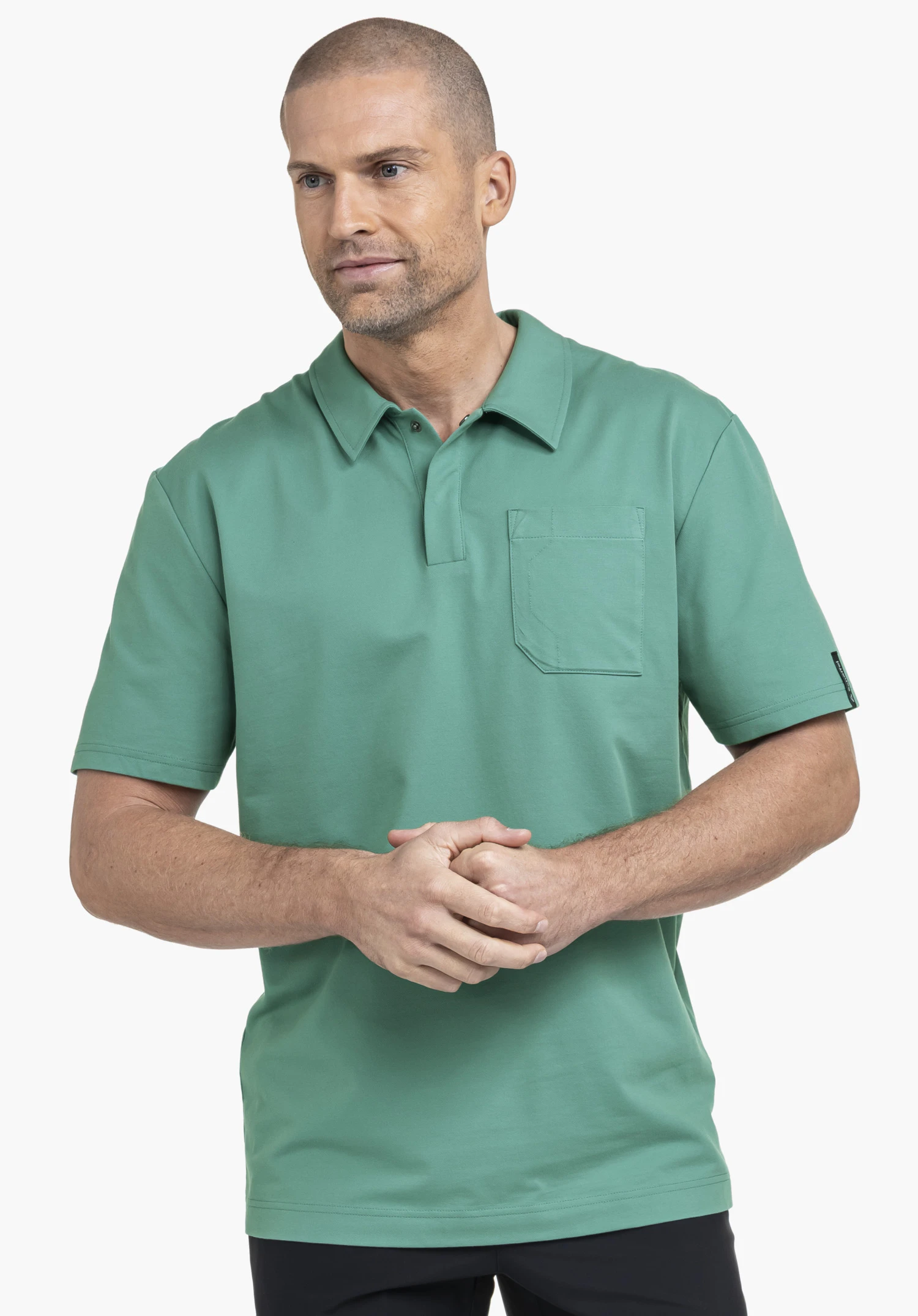 Polo Shirt Style Serenio MEN de couleur verte. Le mannequin se tient de face, les mains croisées devant le corps, et présente la chemise avec un col polo, une poche poitrine et un discret logo Schöffel sur la manche gauche sur un fond neutre.