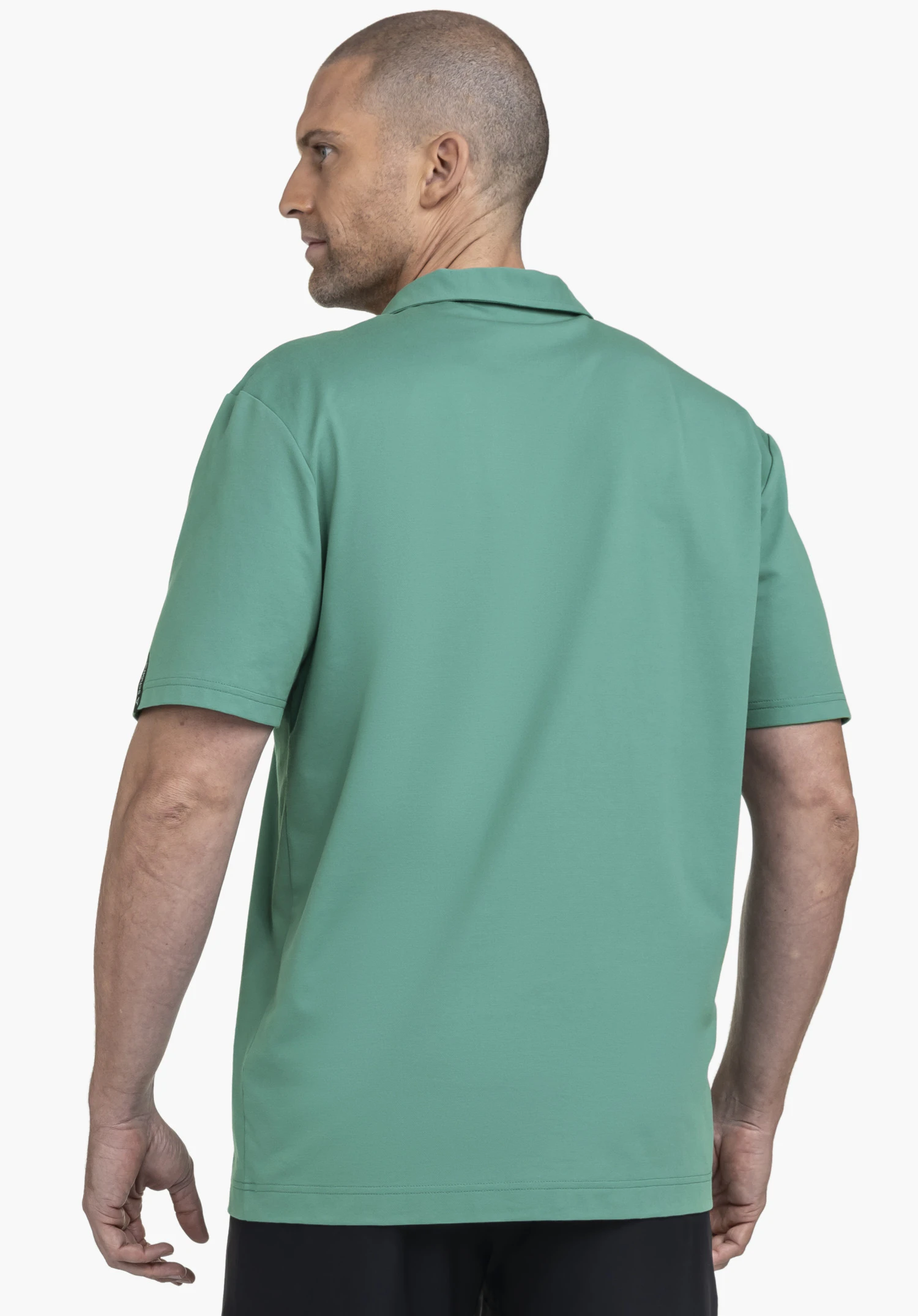 Polo Shirt Style Serenio MEN en vert, présenté dans une vue de dos. Le mannequin est légèrement tourné sur le côté devant un fond neutre. Le logo Schöffel discret sur la manche souligne le look qualitatif adapté à toutes les occasions.