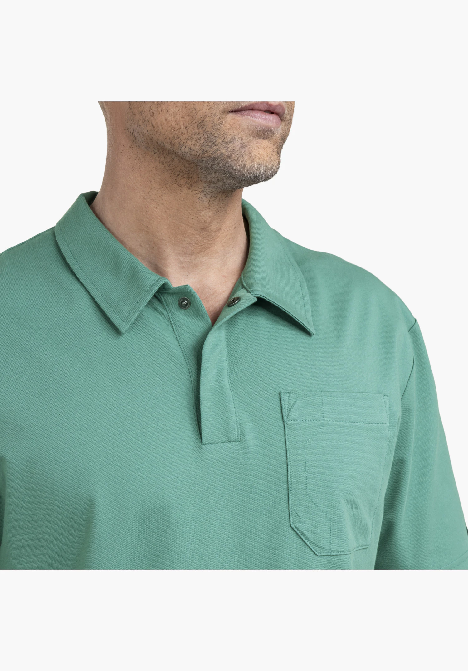Polo Shirt Style Serenio MEN montre les détails du col classique, la patte de boutonnage ouverte avec des boutons foncés et la poche poitrine plaquée sur le tissu vert finement structuré. Gros plan sur fond blanc.