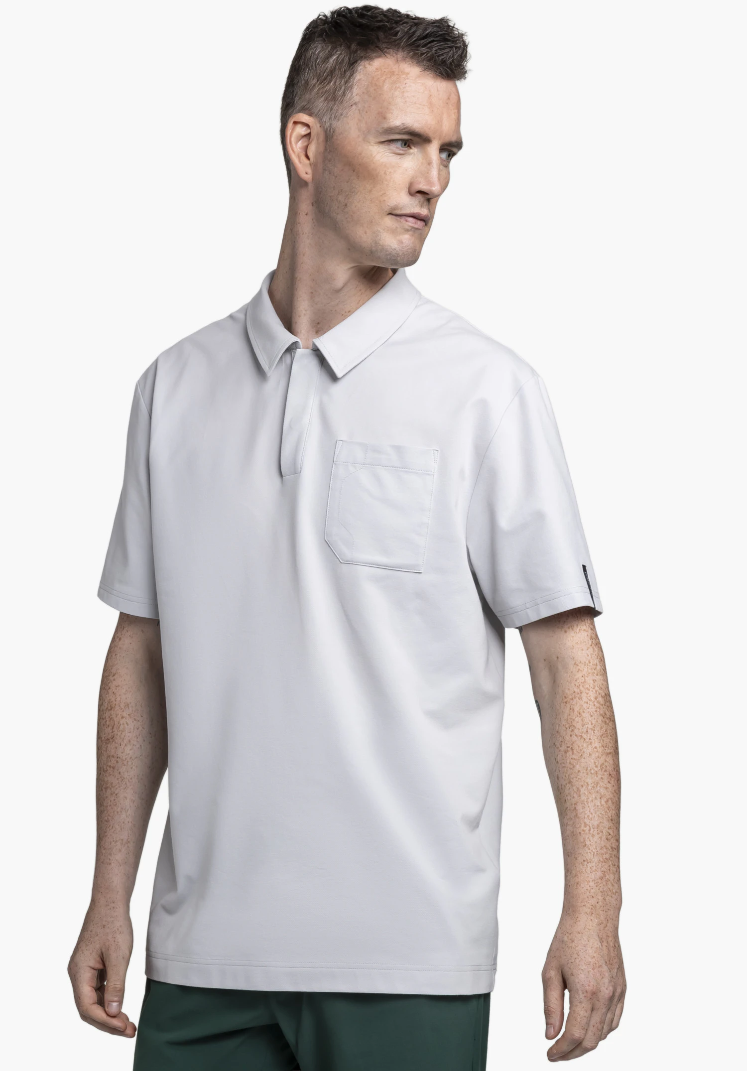 Polo Shirt Style Serenio MEN in grey. A model is wearing the short-sleeved polo shirt with a chest pocket, standing slightly to the side and looking away against a neutral background.