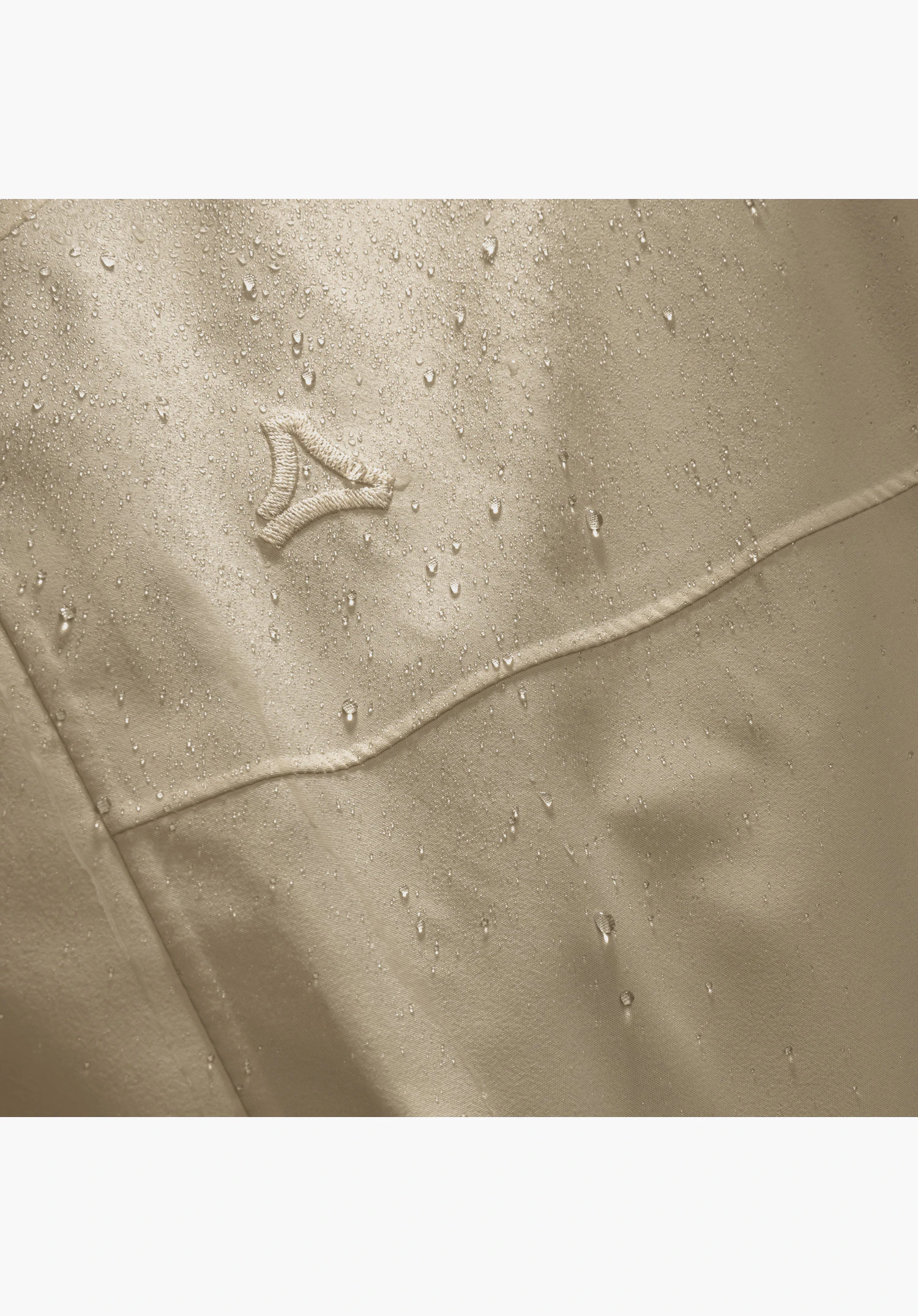 CIRC Jacket Style Smue MEN. Seen here are water droplets beading on the beige fabric and the embroidered Schöffel logo. Close-up against a white/neutral background.