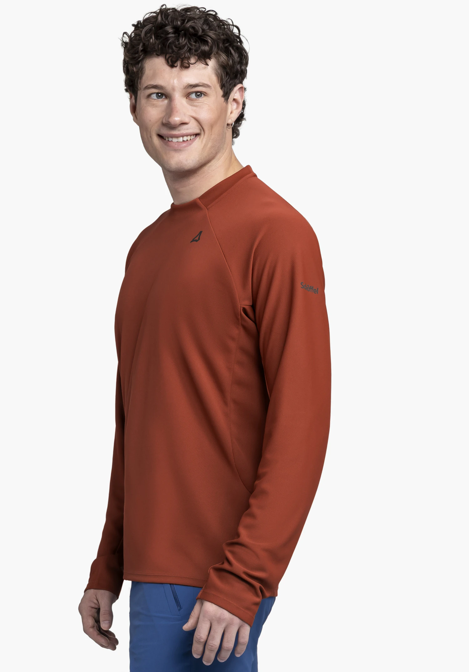Longsleeve Style Enixa MEN en rouge : Un mannequin pose de profil devant un fond neutre avec un sourire. Le haut présente un petit logo Schöffel sur le haut du bras ainsi qu'un logo de la marque discret sur la poitrine.