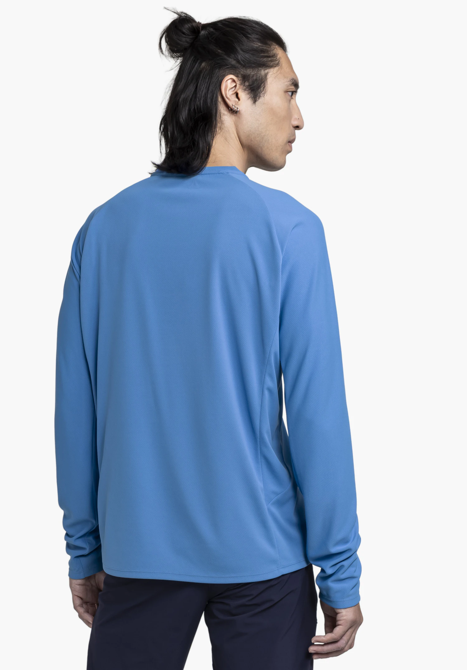 Longsleeve Style Enixa MEN in blue. The model is shown from the back with their head turned slightly, captured against a neutral background to highlight the fit of the functional shirt.