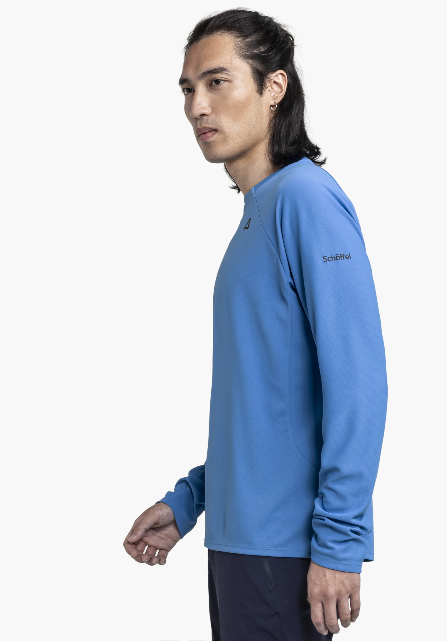 Longsleeve Style Enixa MEN in blue. The model is standing sideways against a neutral background, showcasing the long-sleeved shirt with the Schöffel logo clearly visible on the sleeve.