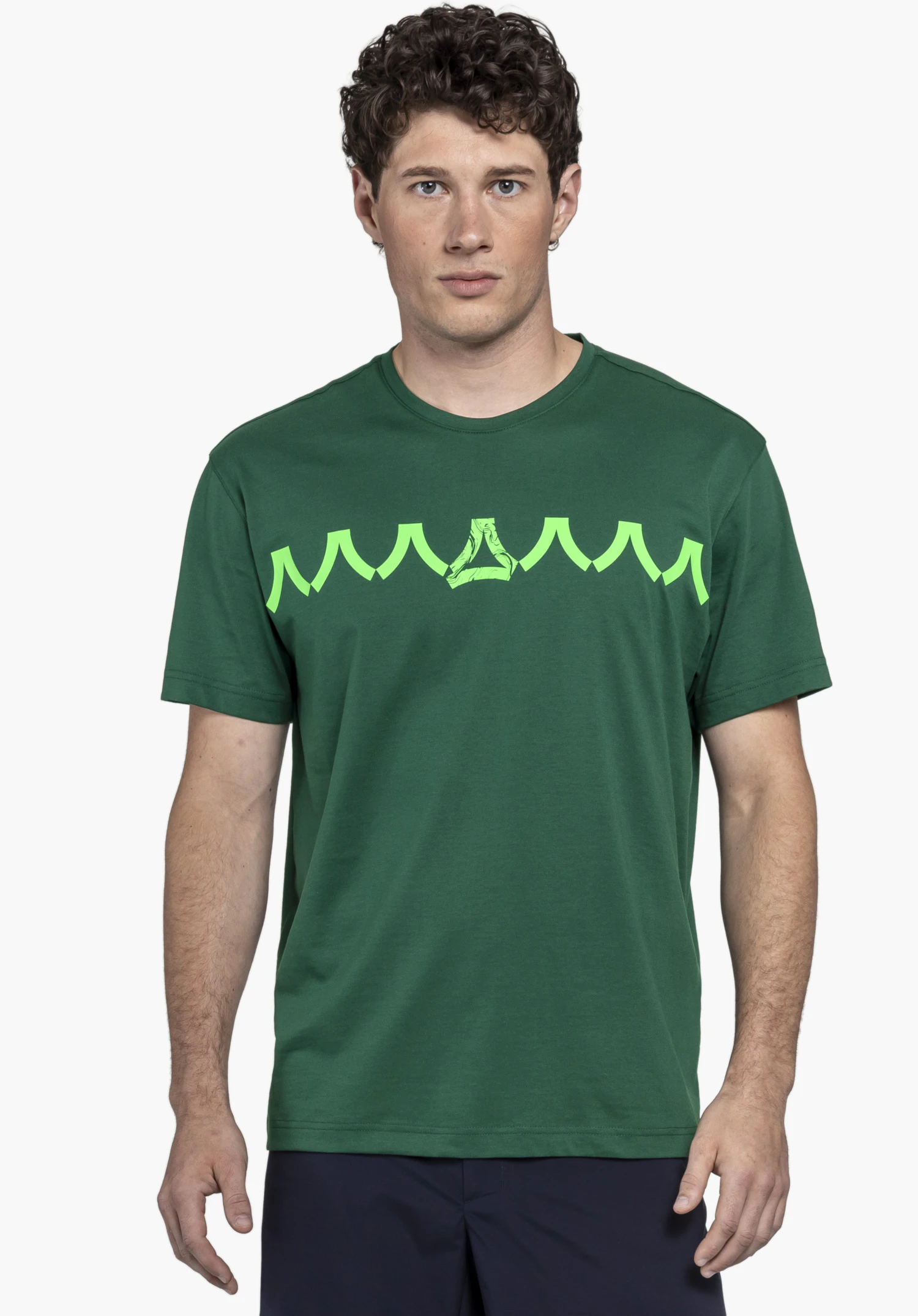 T Shirt Style Elmori MEN. Le mannequin pose de face devant un arrière-plan neutre, vêtu du t-shirt dans un vert intense. Un imprimé graphique distinctif orne la poitrine, tandis que le logo Schöffel discret complète le look sportif.
