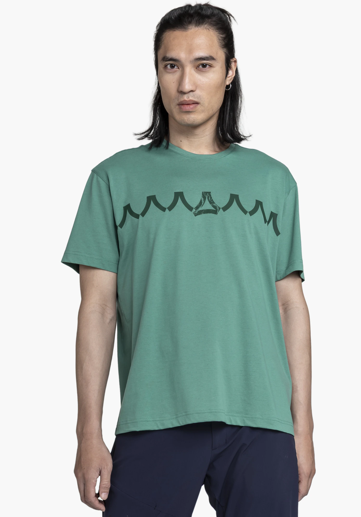 T Shirt Style Elmori MEN in green. A model stands frontally against a neutral background, showcasing the shirt featuring a striking graphic Schöffel logo on the chest.