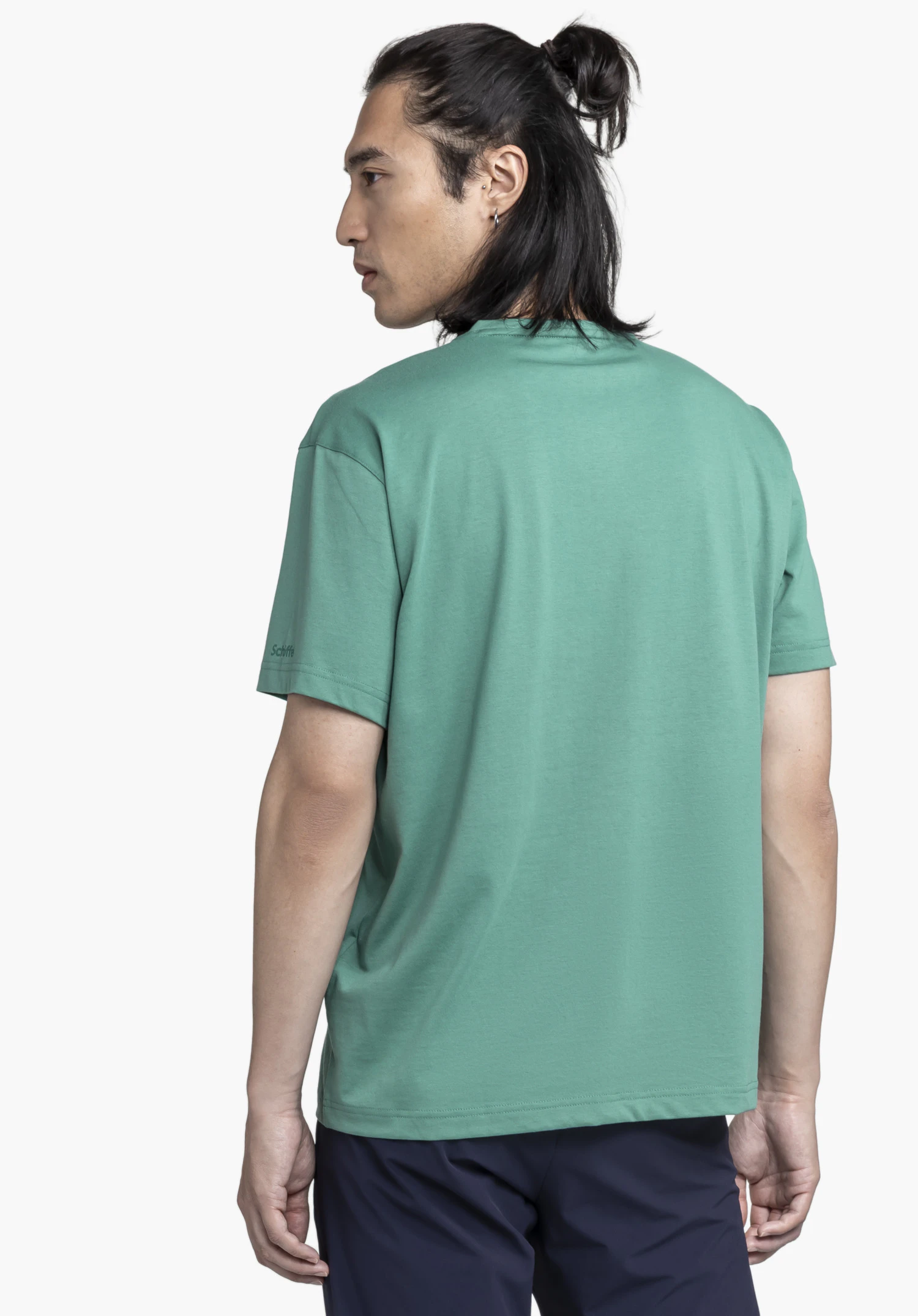 T Shirt Style Elmori MEN. A model wears the green t-shirt in a back view, looking slightly to the side, with the Schöffel logo visible on the left sleeve. Photographed against a neutral background.