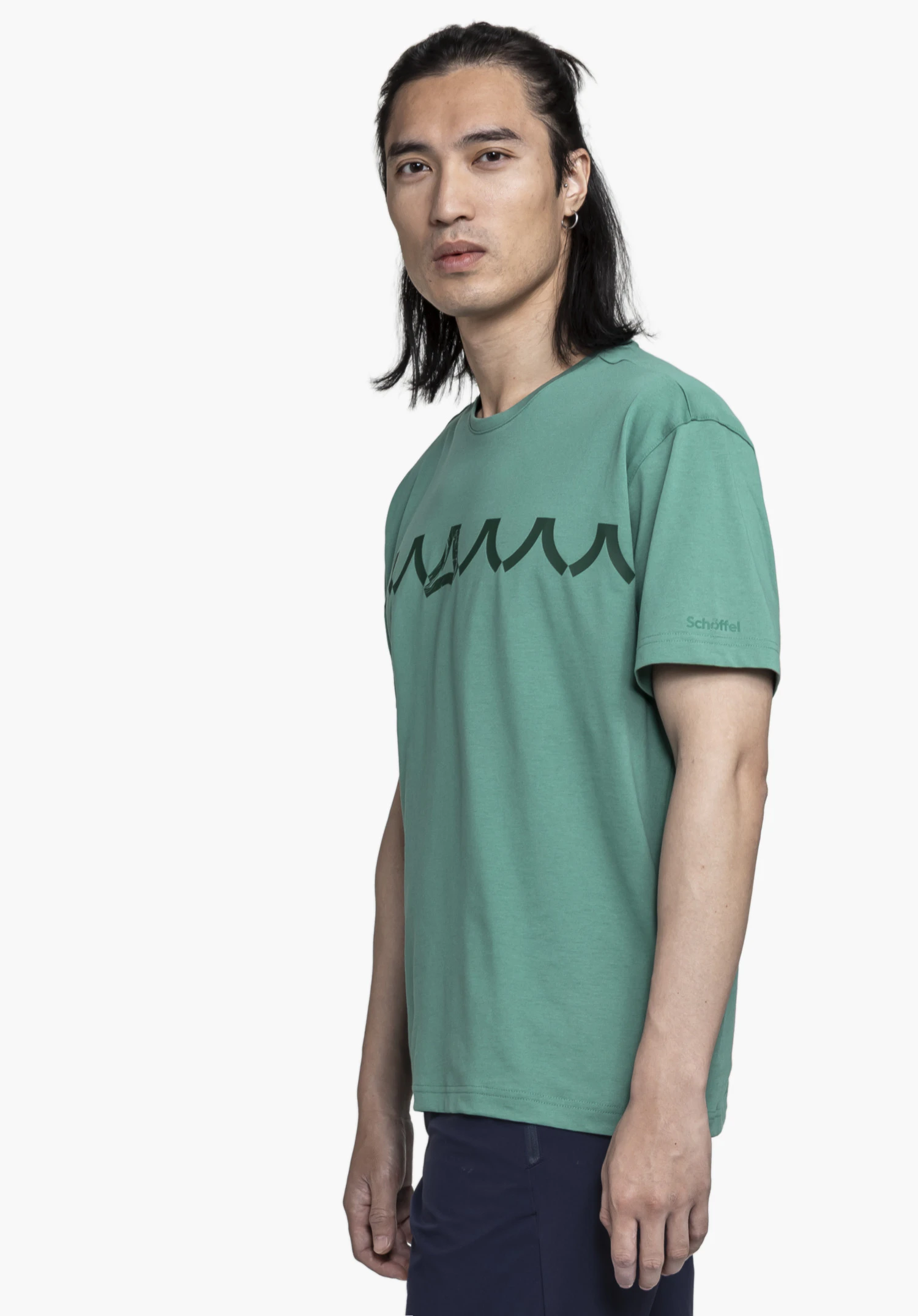 T Shirt Style Elmori MEN in green, shown on a model in a semi-profile pose. Set against a neutral background, the shirt features a bold graphic print and the subtle Schöffel logo on the sleeve.