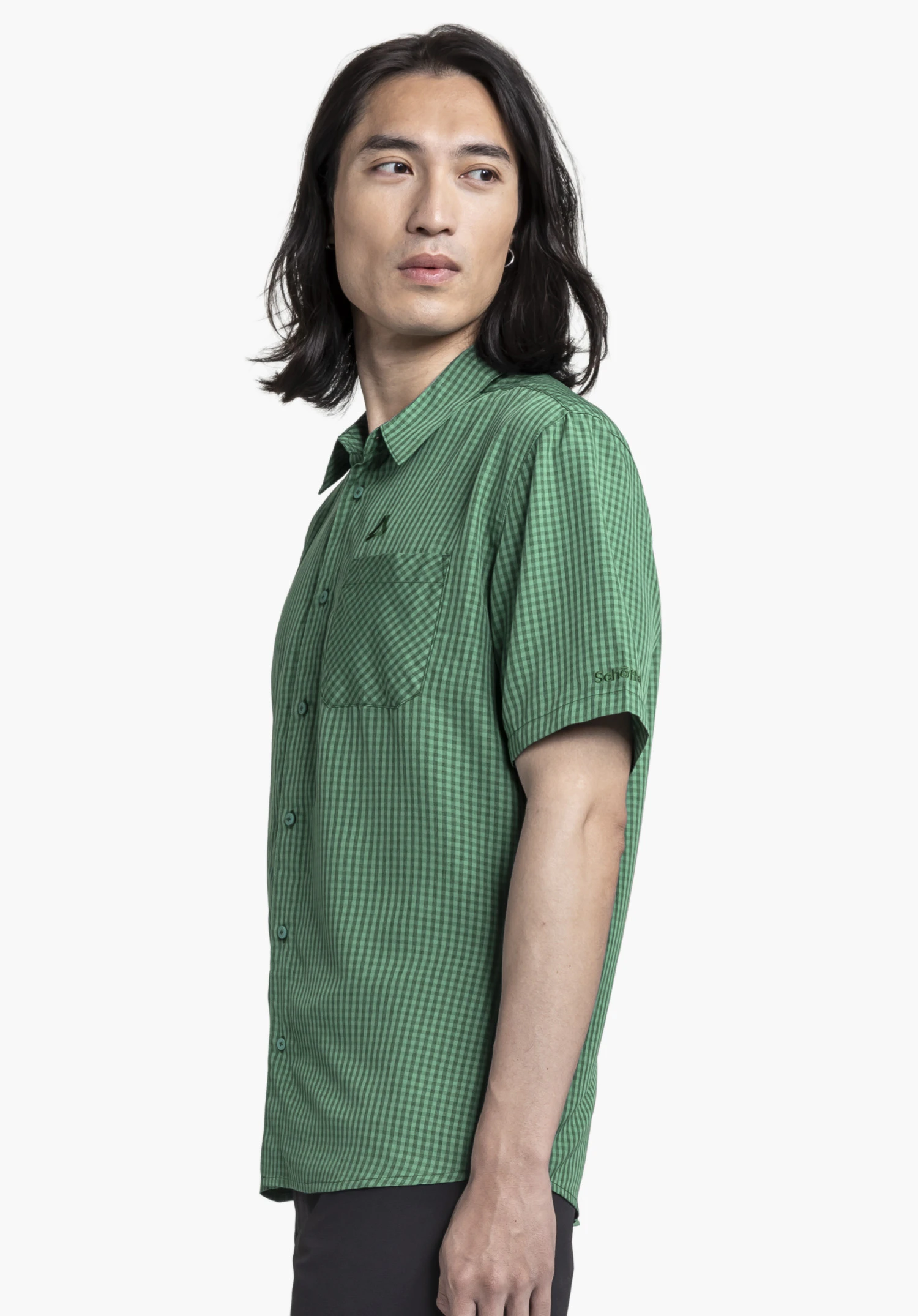 CIRC Shirt Style Dalfoss MEN. A model stands sideways wearing the green, short-sleeved chequered shirt. The Schöffel logo is visible above the chest pocket and on the sleeve. The garment is presented against a neutral background.