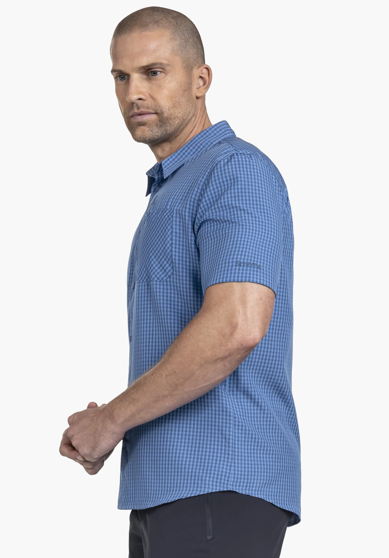 CIRC Shirt Style Dalfoss MEN. A model stands sideways presenting the blue, short-sleeved checked shirt. The Schöffel logo is visible on the left sleeve. The image is taken against a neutral background.