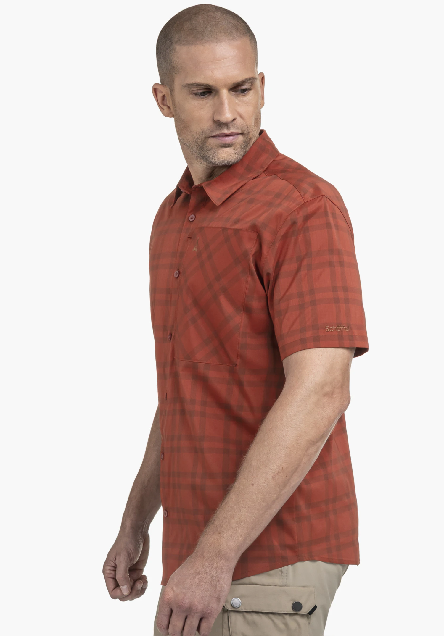 Shirt Style Frolya MEN in red, worn by a model. The man is standing sideways and looking over his shoulder. The checked short-sleeved shirt features a chest pocket and the Schöffel-Logo is visible on the left sleeve. Photographed against a neutral background.
