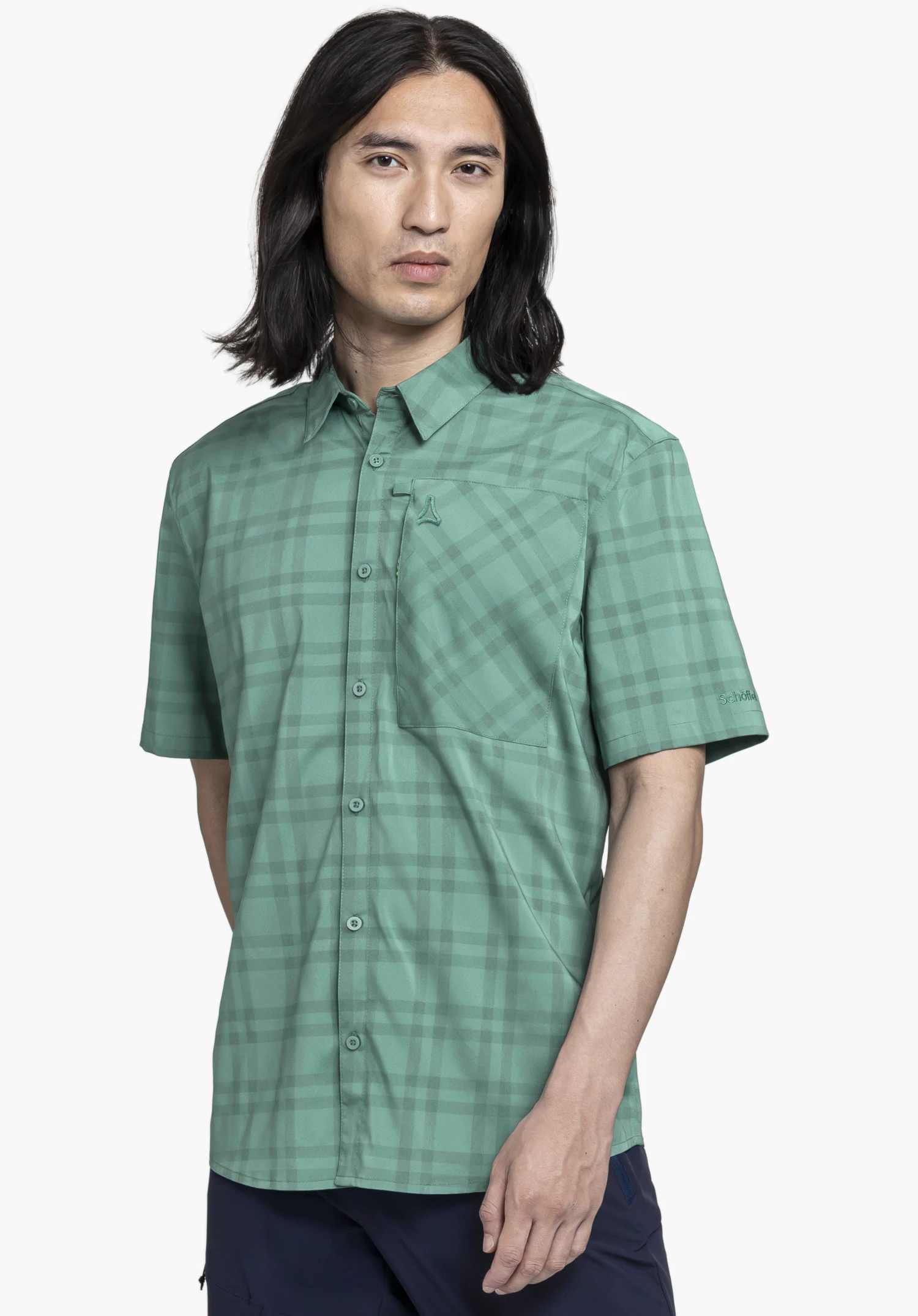 Shirt Style Frolya MEN in green. A model stands frontally against a neutral background, showcasing the shirt with its subtle check pattern. The small Schöffel logo is visible on the chest pocket, as well as a subtle Schöffel logo on the sleeve.